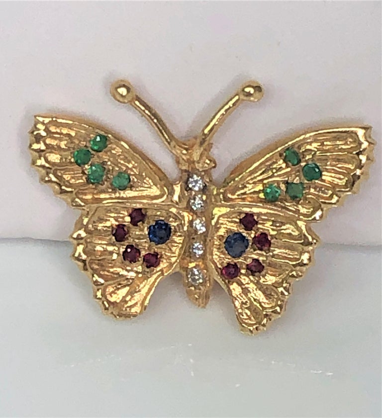 14 karat yellow gold butterfly, approximately 19mm x 24.5mm.
5 total round diamonds- down the abdomen of the butterfly.
8 total round emeralds- four on each wing.
8 total round rubies- four on each wing.
2 total round sapphires- one on each