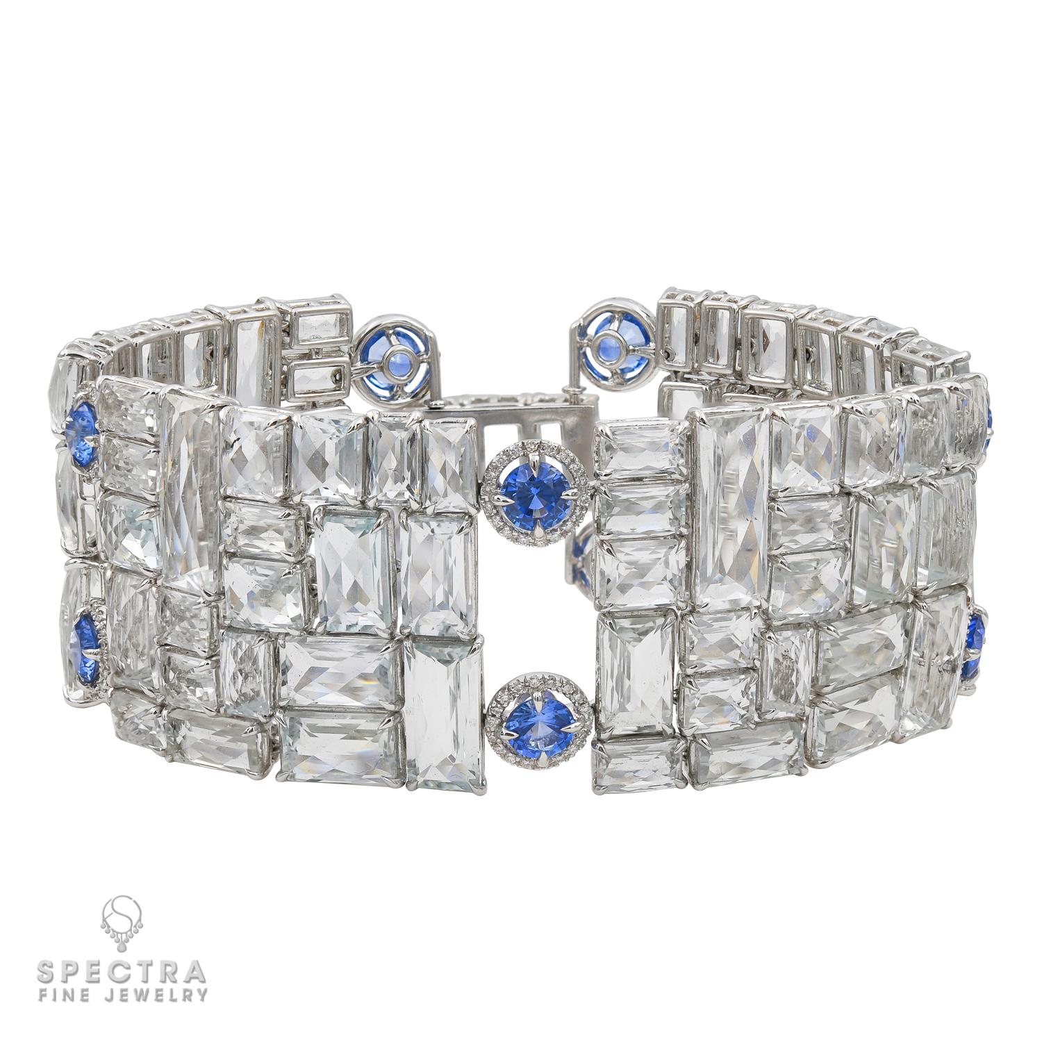 Crafted in 18K white gold, this Contemporary Diamond, Sapphire, and Topaz Articulated Bracelet channels the elegance of the Art Deco era. Comprising four articulated links set with rectangular faceted white topaz and encircled by circular-cut