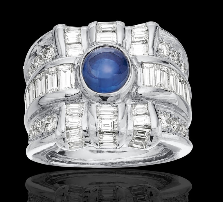 Stunning 18ct diamond and sapphire ring. Design as a present/gift motif as there's two criss crossing rows of glistening baguette cut diamond with an eye catching round cabochon cut sapphire at the center. 
1 x sapphire approximate weight 2.0