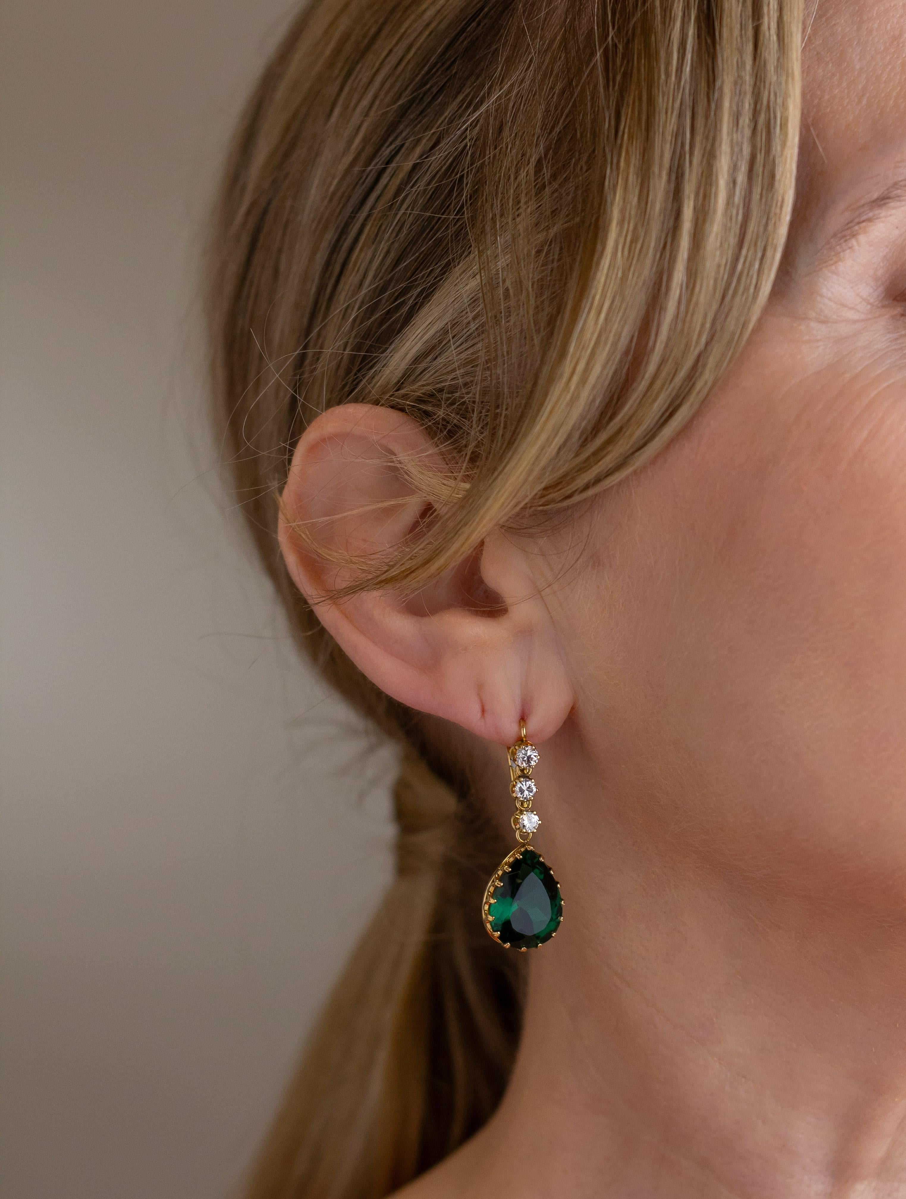 Fabriquée en or jaune 18 carats et sertie de diamants, cette paire de boucles d'oreilles pendantes est ornée d'un quartz vert synthétique en forme de poire. Les crochets de berger sont dotés d'un levier qui les maintient en place sur l'oreille et