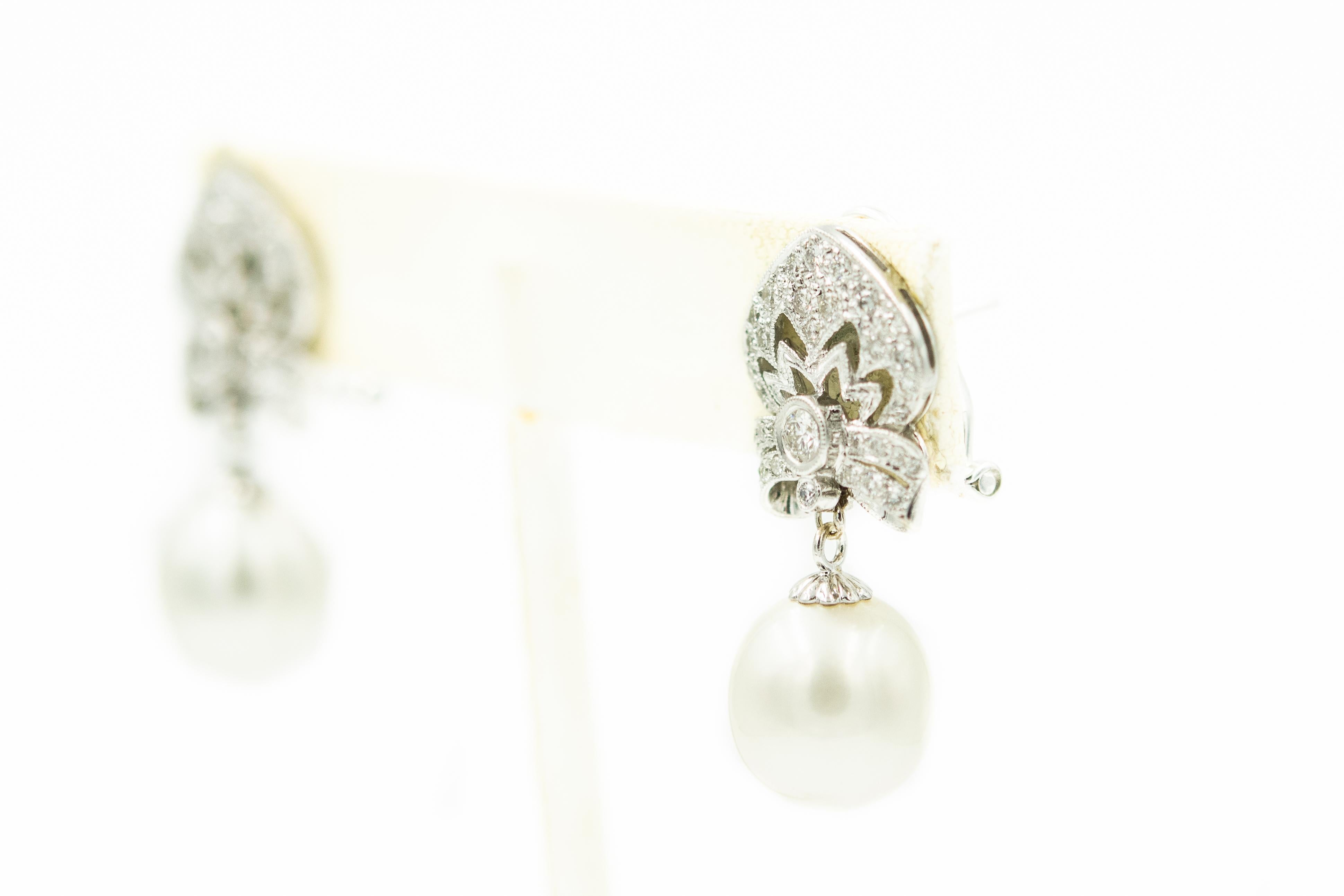 Beautiful 18k white gold dangle earrings featuring a 12mm silvery white cultured pearl drop originating from a diamond top shield motif section. They have omega post backs. Marked 750 MC The approximate total diamond weight is .74 carats.