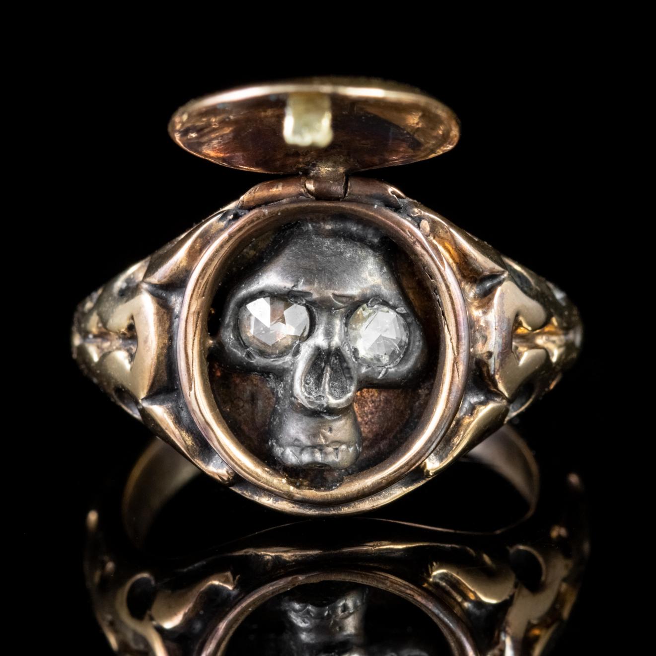 This ingenious ring has been crafted in the Georgian Memento Mori style. 18ct Yellow Gold has been skilfully worked into a sturdy clasped locket, with beautiful engravings wrapped around the ring’s shoulders.

Within the locket is a stylised Silver