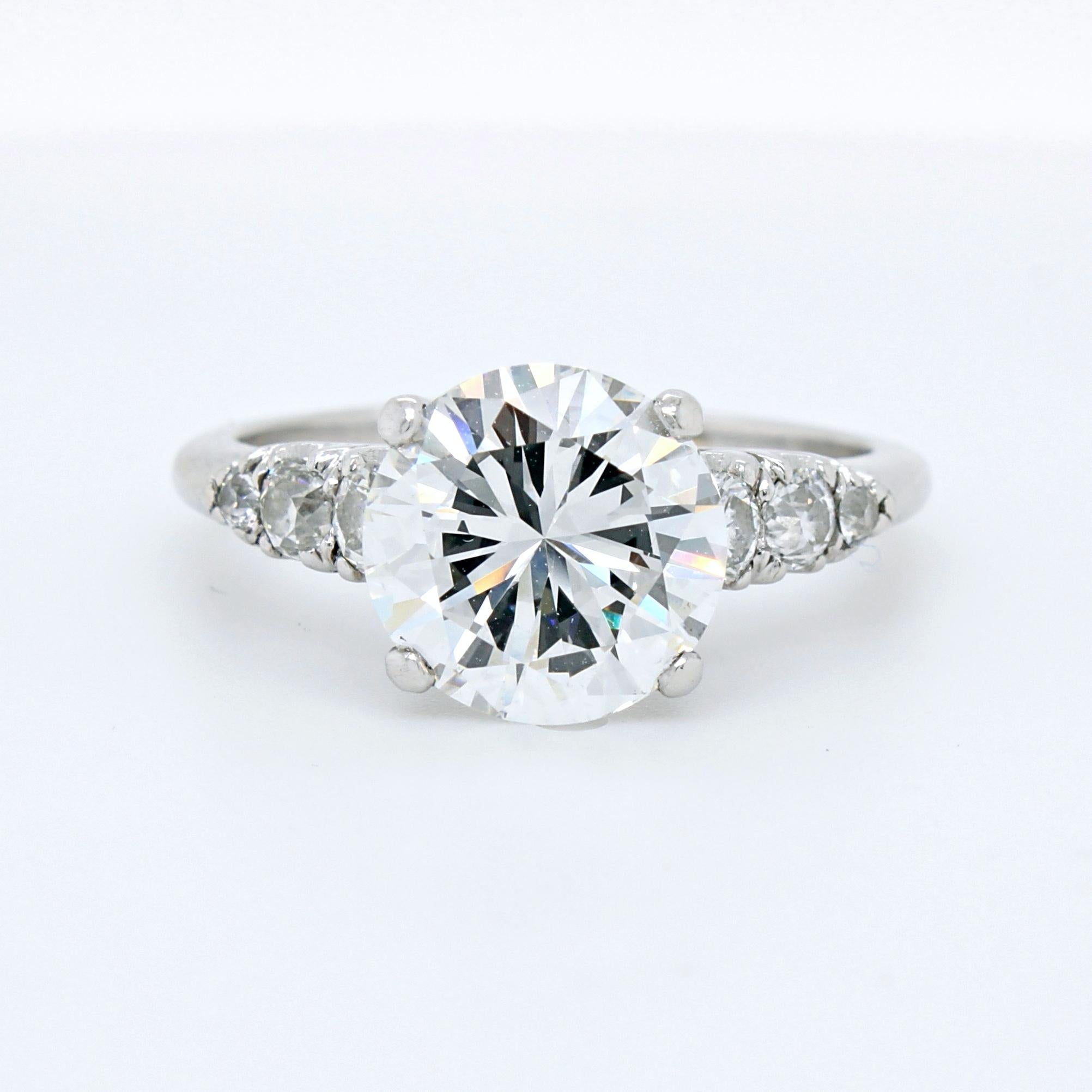 A diamond round brilliant solitaire ring in platinum. The centre diamond weighs 2.72 carats, G colour - VS2 clarity, certified by GIA. It is flanked by three smaller round brilliant cut diamonds on each side.

The design of the ring is very elegant