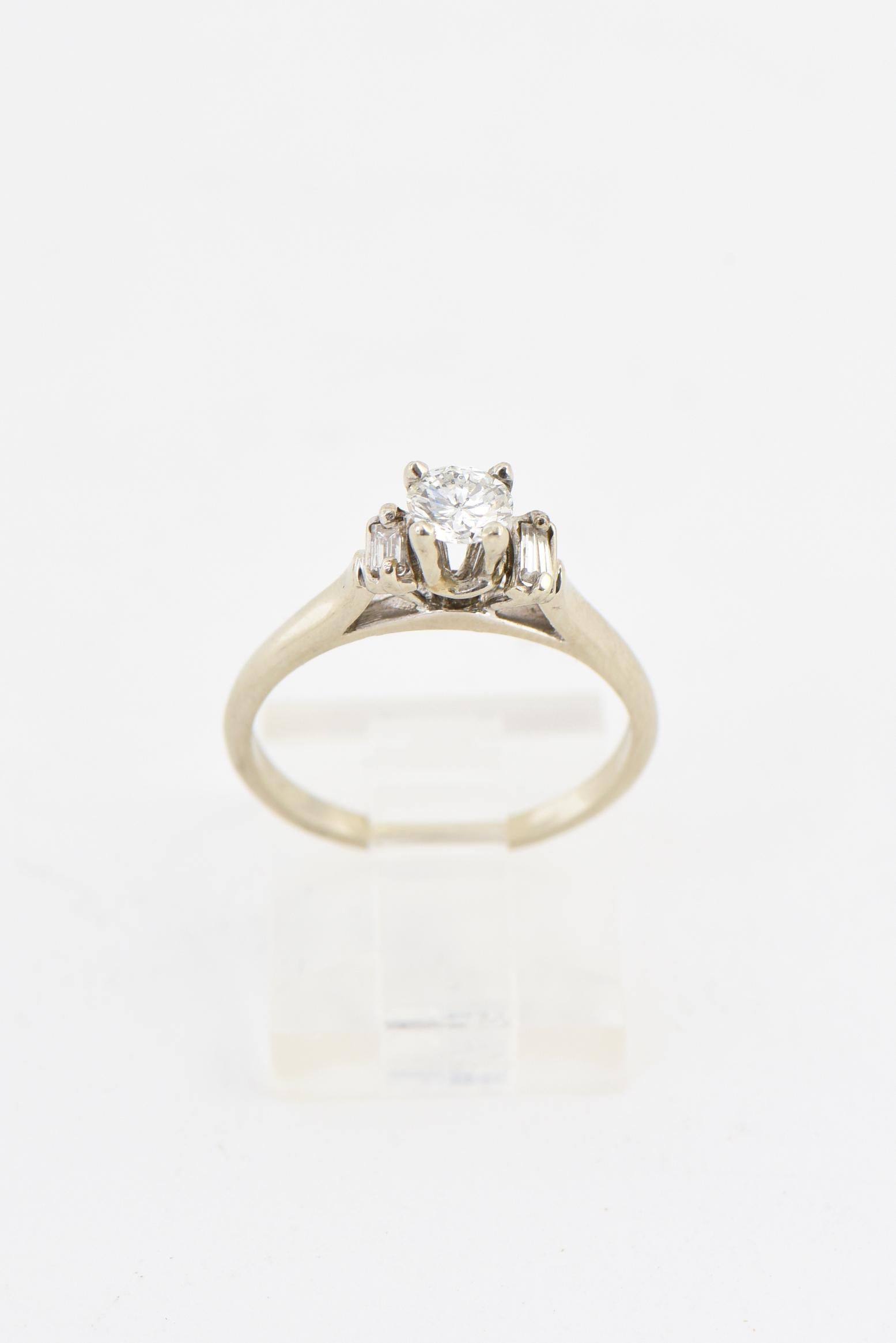 Elegant 14K white gold ring presenting a .35 carat diamond mounted in a traditional four-prong setting flanked by a baguette-cut diamond on each side. Center diamond, H-I color - SI. Age wear. US size: 6.25; can be sized. Marked: 14K.
