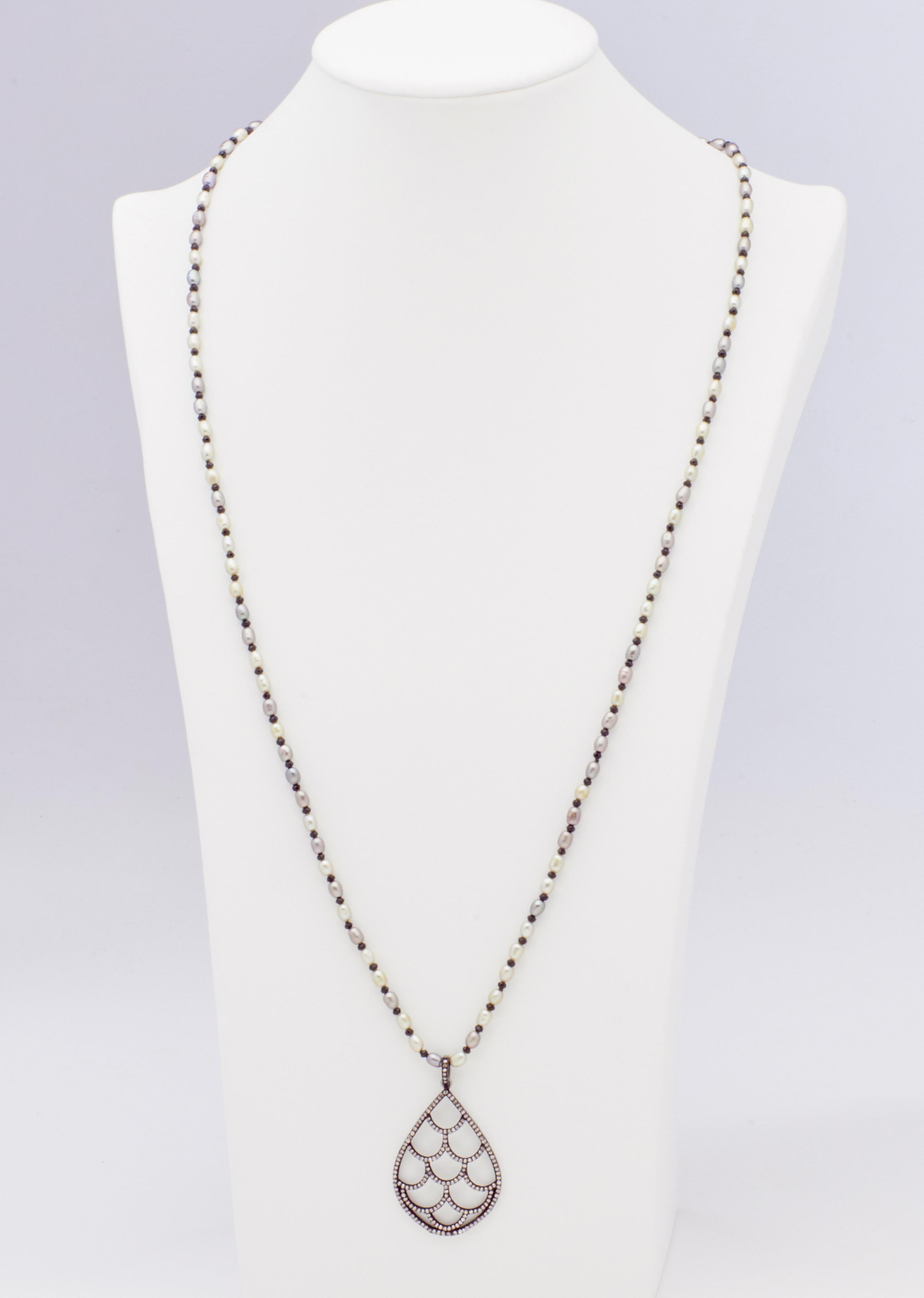 A cascading sterling silver tear drop pendant charm glistening with diamonds suspended on a 26 inch necklace strand of  3.5mm light gray Akoya button pearls offset by 2.5mm natural spinel beads to create a light fresh look perfect to display on a