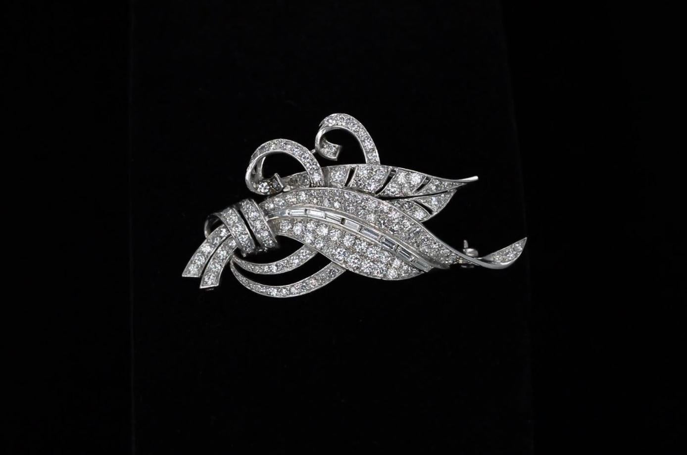 The graceful curves of leaves and flowing ribbons glint and gleam in this estate diamond brooch. The pin contains approximately 128 round and 8 baguette diamonds altogether weighing approximately 3.00 carats. The diamonds have an average color of F