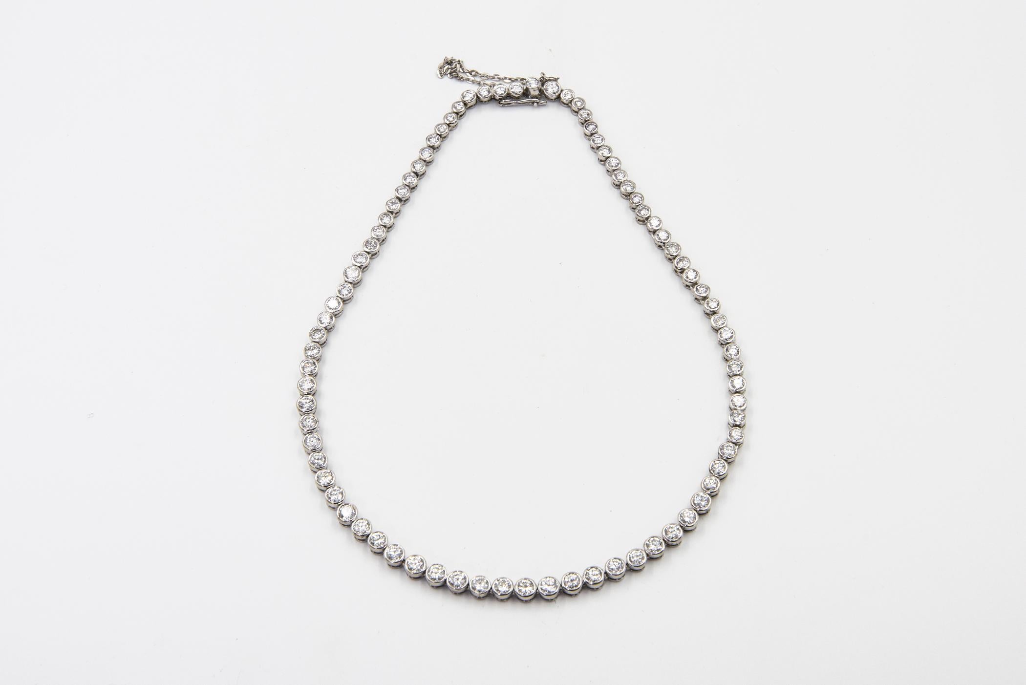 Graduated natural diamond tennis necklace mounted in 14k white gold.  There are 80 bezel set diamonds. It has an approximate total weight of 9 carats in diamonds.  The clasp is a push button with a safety chain.  This necklace is only shorter than