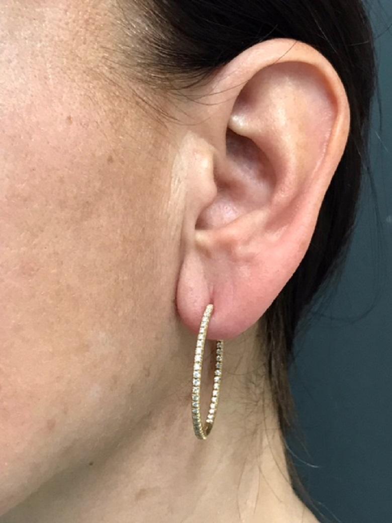 A pair of Tiffany & Co. 18k gold hoop earrings with diamonds, from the Tiffany Metro collection.  
The diamonds are set along the curves. They staged both on the outside and inside, on the back of the hoop. The hoops are smooth and round-edged. They