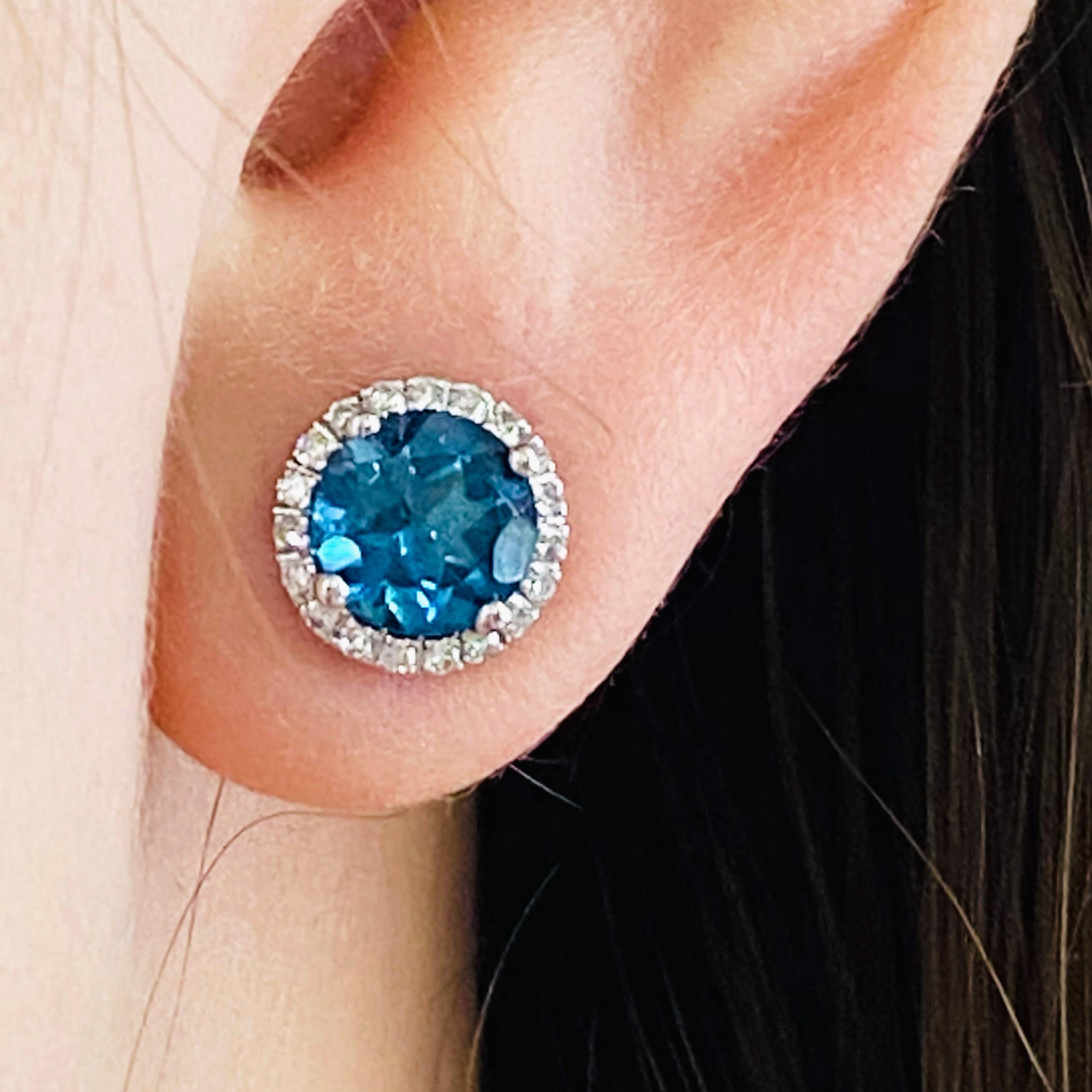 This London blue topaz and diamond halo earrings are a modern design set in 14 karat white gold! Each earrings holds a round, genuine London blue topaz gemstone set in four white gold prongs. The London blue topaz is framed with bright white, round