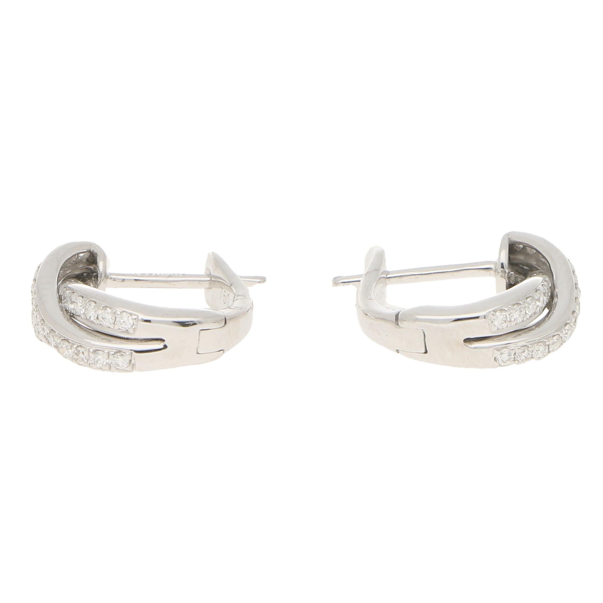 A lovely pair of diamond trinity huggy hoop earrings set in 18k white gold.

Each earring is composed of three intertwining white gold bands, all of which are pavé set with round brilliant cut diamonds. Each hoop is fastened with a hinged post clip