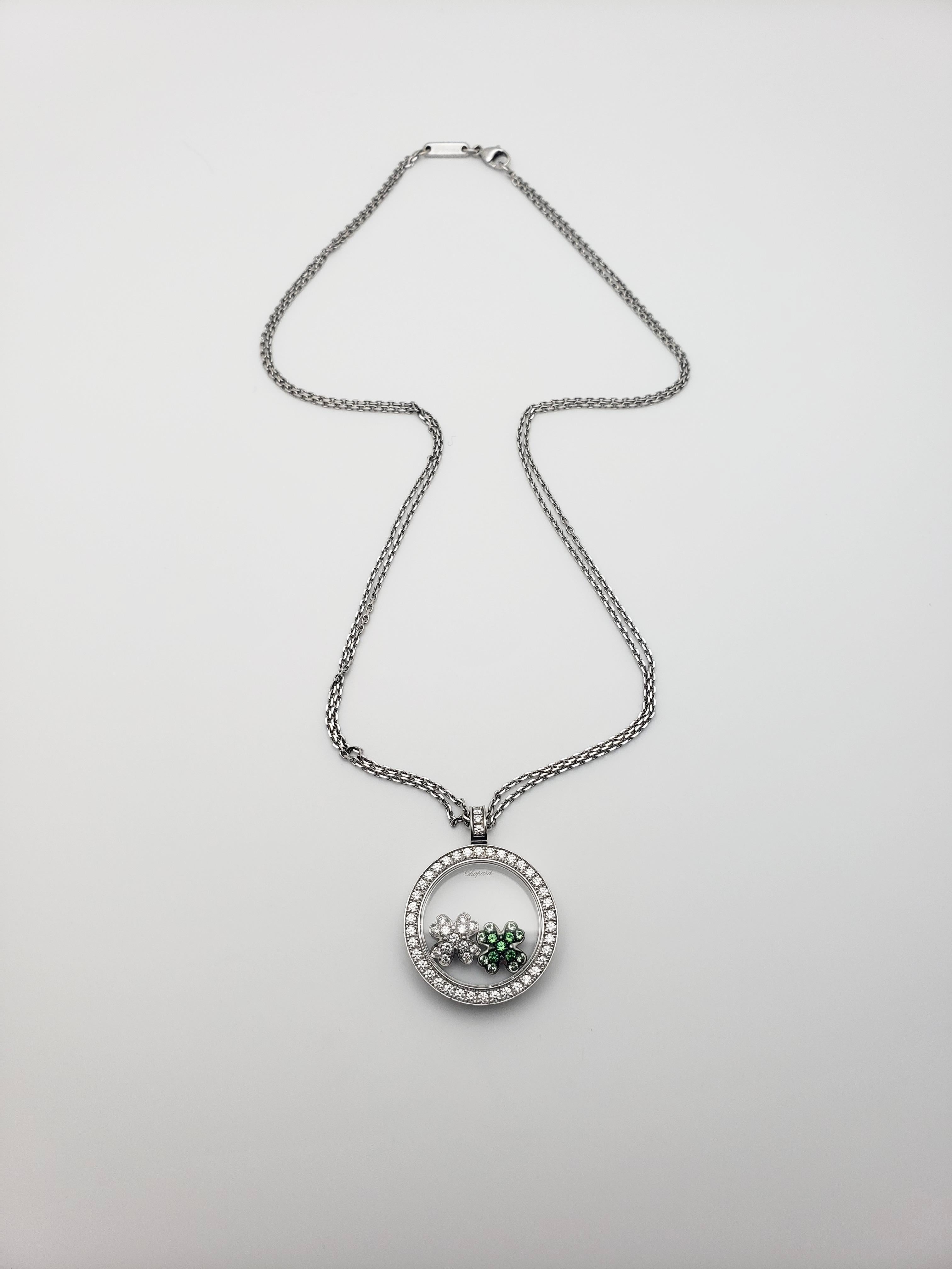An authentic 18K white gold double chained diamond pendant, with happy diamond Irish clovers sealed within a double sided see-through natural crystal sapphire (corundum) case. The two happy diamond and graduated green tsavorite clovers move freely