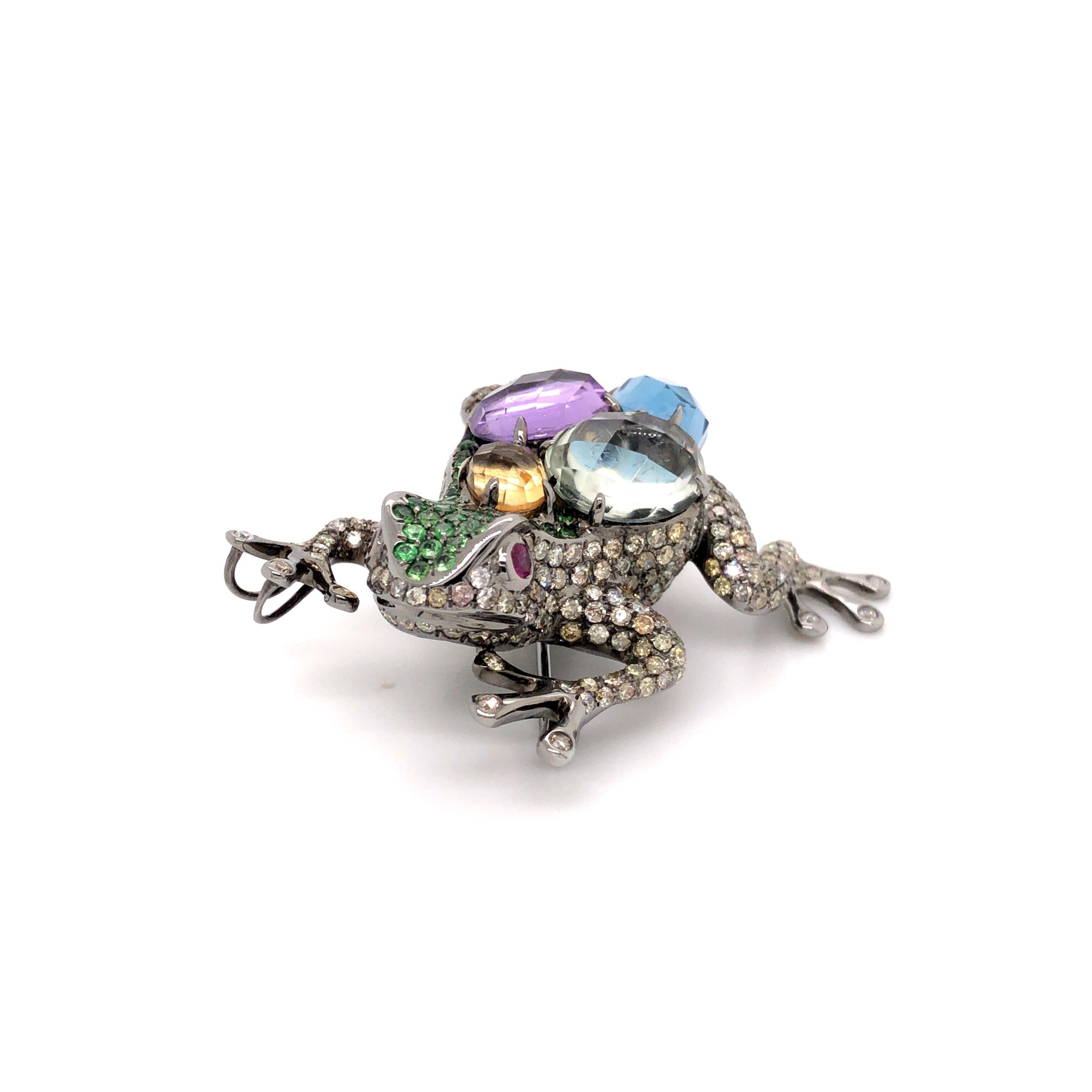 Le pendentif et la broche grenouille dorsale multicolore en diamant, tsavorite et rubis est une pièce fantaisiste et captivante qui capture l'esprit de la nature d'une manière unique. Le pendentif et la broche sont ornés d'une grenouille au design