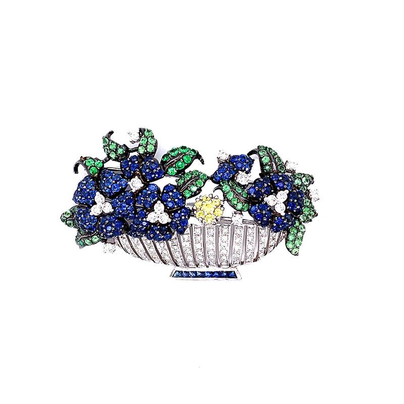 A lovely brooch of gem-set flowers inside a gold diamond studded vase. This piece features a total of 6 carats of diamonds, tsavorite, blue sapphire and fancy yellow diamonds. They are set in 18k white gold and ready to be worn on your next