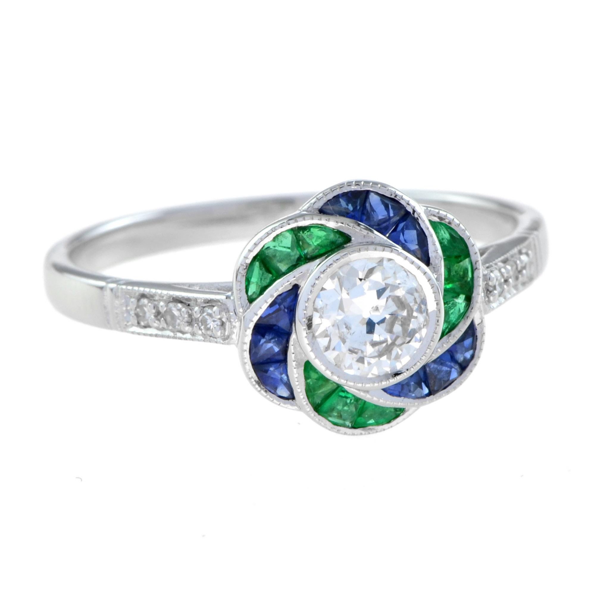 Artistry and sophistication come together in a flower ring with diamond, emerald, and sapphire from the Art Deco era. The ring features a round shape center diamond in a bezel setting surrounded by French cut blue sapphire and emerald for its
