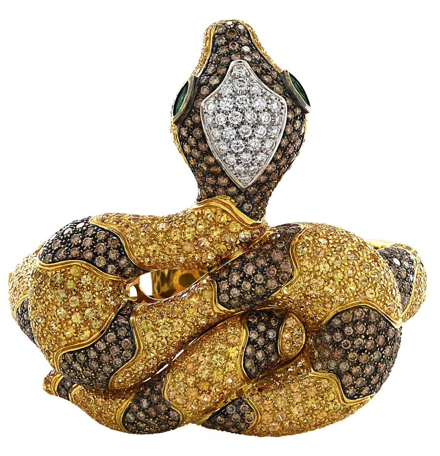 Stunning snake bangle crafted in 18 karat yellow gold, encrusted with 583 yellow sapphires weighing approximately 29.2 carats total, 408 round cut white and brown diamonds weighing approximately 12.6 total and 2 marquise cut emeralds weighing