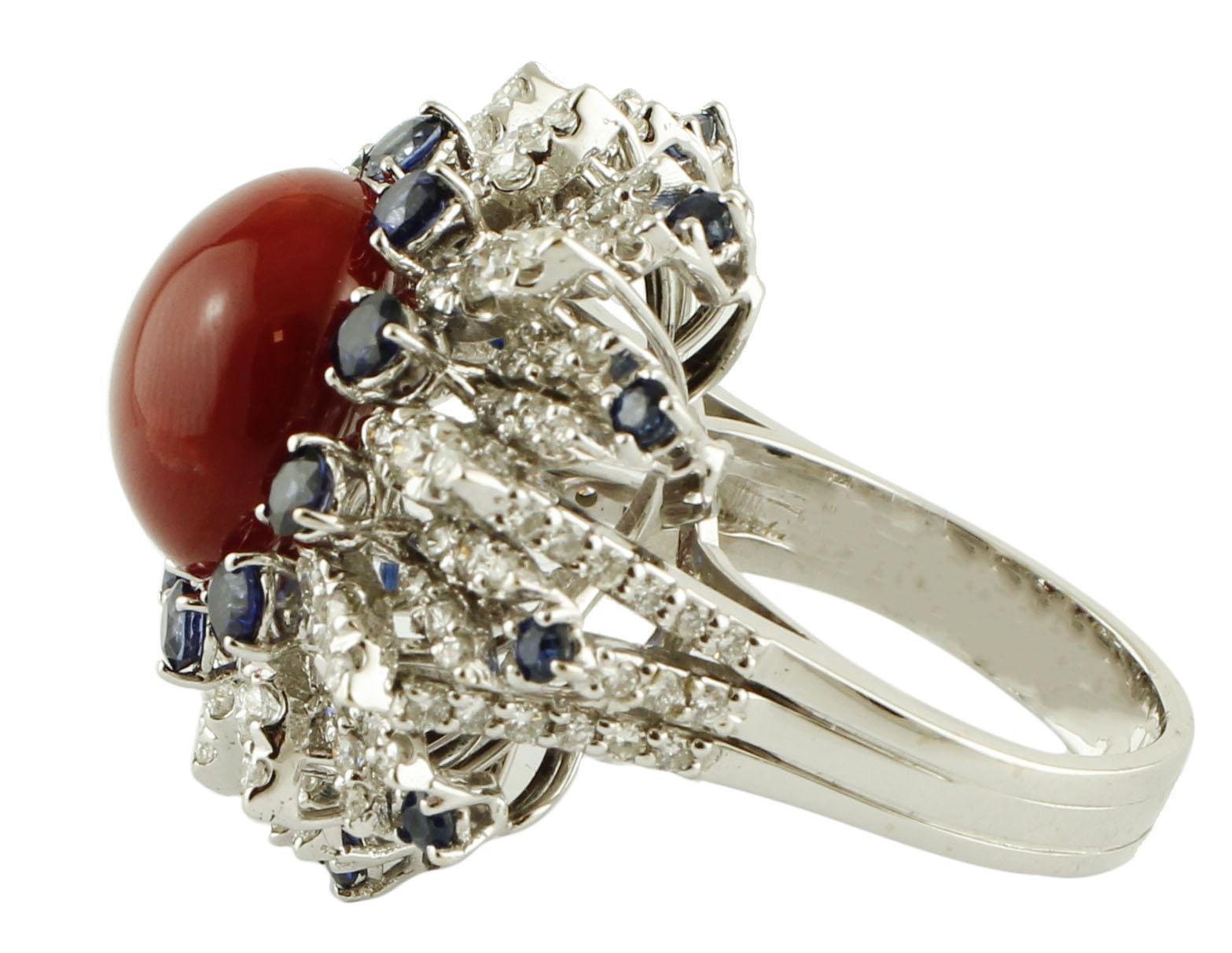 Astonishing ring in 14k white gold, mounted with a central oxblood coral sphere surrounded by a crown of intense blue sapphires and by white gold leaves studded with diamonds. 
This ring is totally handmade by Italian master goldsmiths
Oxblood Coral