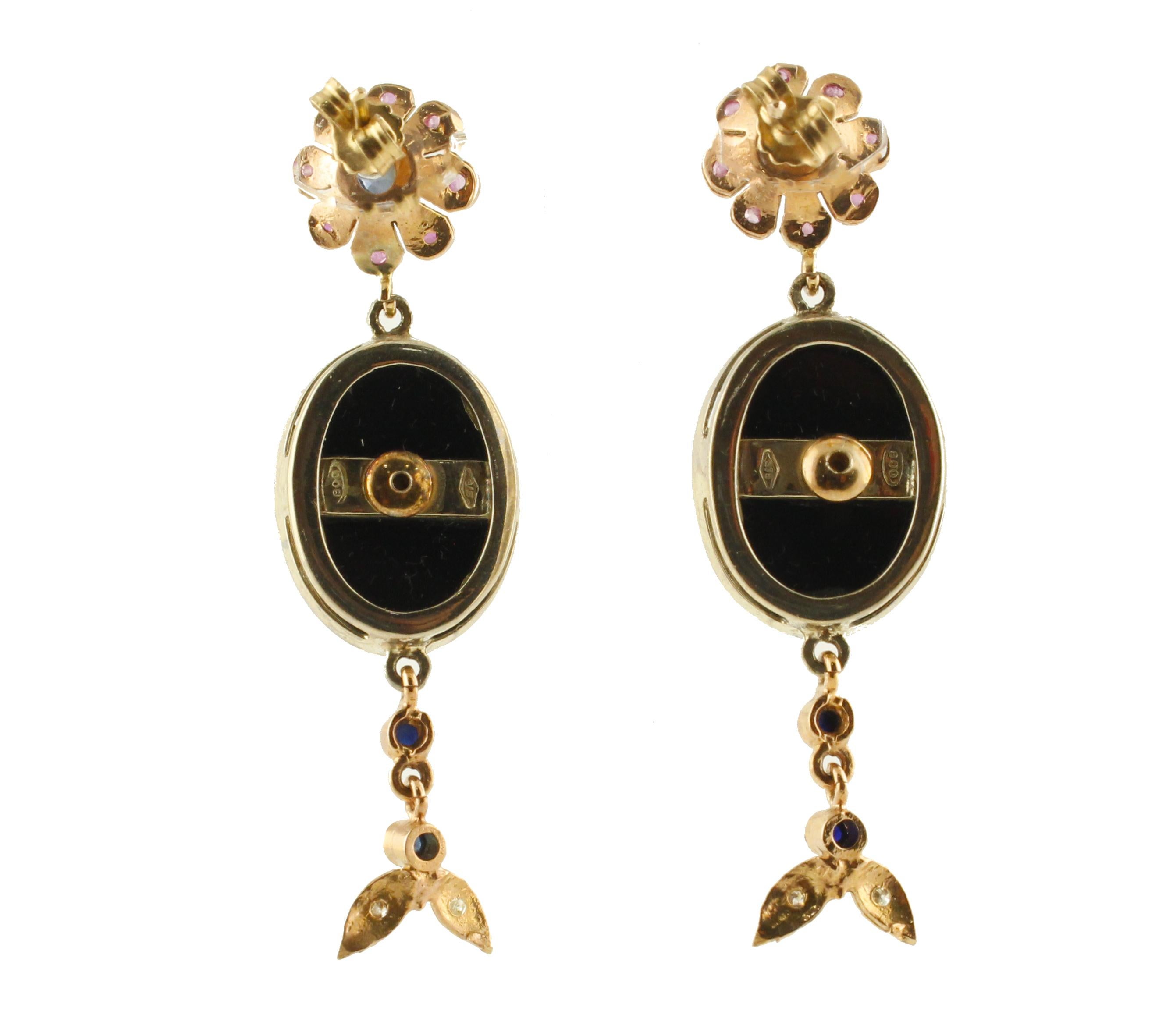 Elegant earrings in 9K rose gold and silver structure, composed of blu sapphires and rubies flowers at the top of the earrings, in the middle there are two onyx botton with a rose gold flowers and diamonds in the center. At the bottom of the