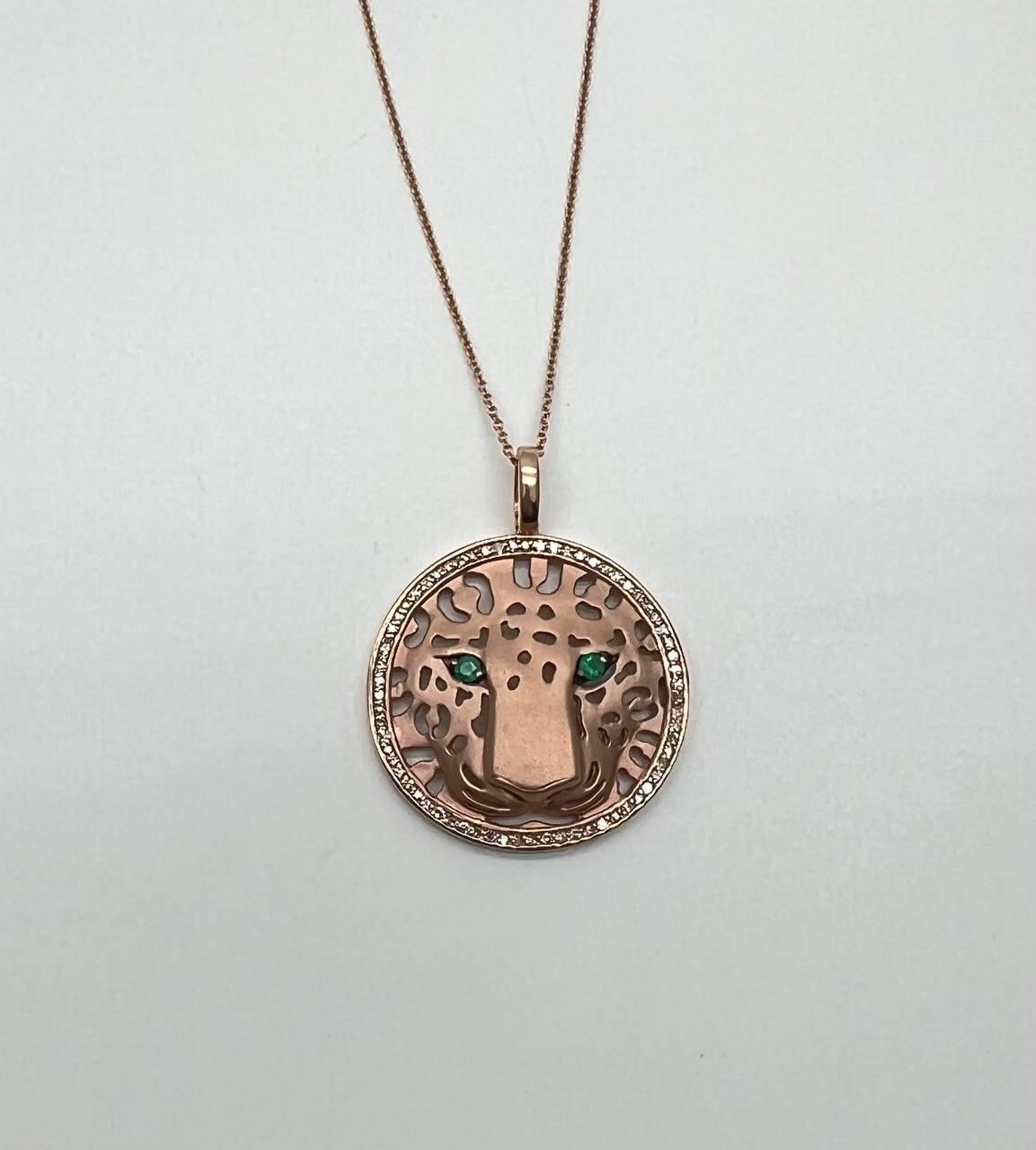 A captivating pendant necklace featuring a leopard motif with intricate cut-out details. The eyes are adorned with vibrant green emeralds, set in a warm-toned metal. The pendant is encircled by a delicate border of accented white sparkling diamonds,