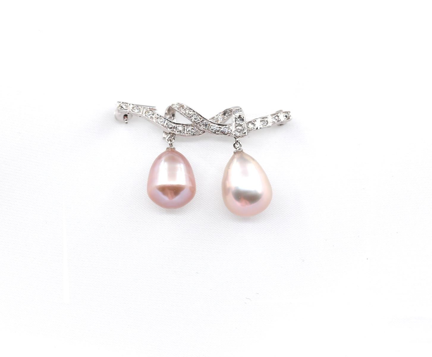 A Vintage Diamond And Pearl Brooch in 18 Karats White Gold. Designed as a lover's knot set with old cut Diamonds suspending two Pink Pearl drops. One Pearl is slightly more pink in shade, representing a woman and the other one is more of a silver