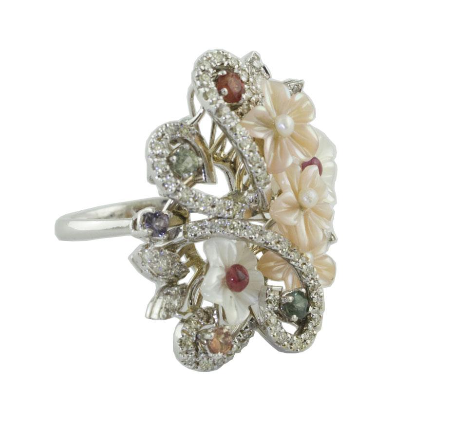 Fashion ring in 14K white gold ring composed of mother-of pearl flowers embelished by little pearlsand studded by diamonds and multi-color sapphires
Diamonds 0.65 ct 
Multi-Color-Sapphires 0.68 ct 
Little Pearls 0.10 g
Mother-of-pearls 0.60 g 
Total