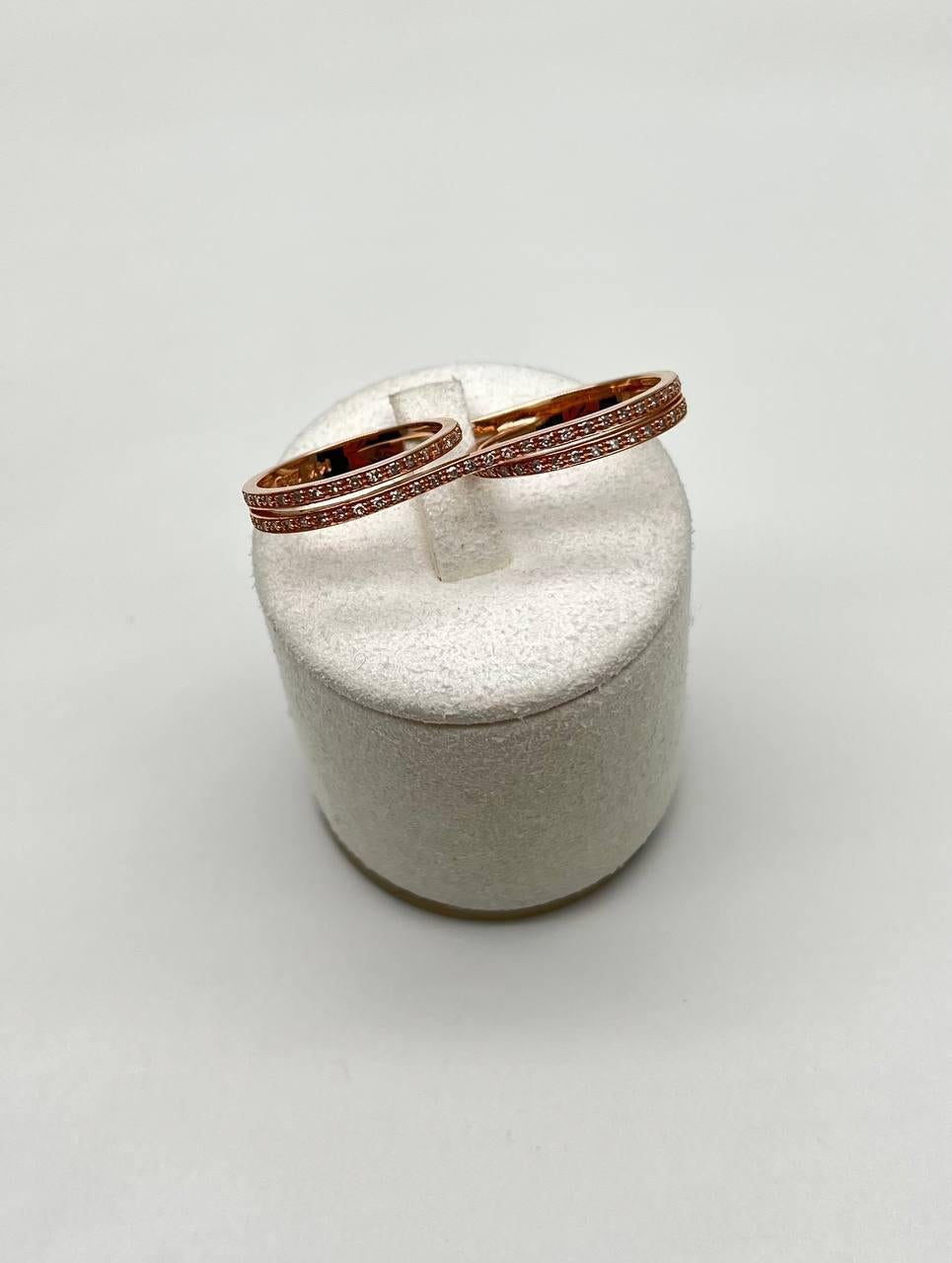 Questo squisito anello presenta un design elegante realizzato in una calda tonalità oro rosa. Ogni anello è ornato da una delicata fila di pietre scintillanti, meticolosamente incastonate per catturare la luce da ogni angolazione. Il design a doppia
