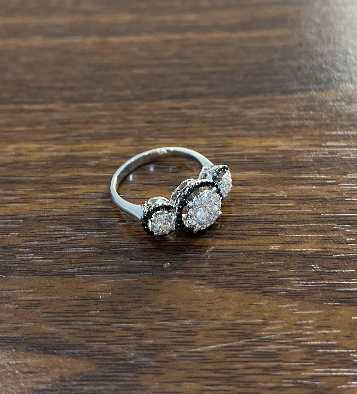 A striking ring from. This exquisite piece features a captivating design with a central round black & white diamonds weighing 1.0 carat. The ring is surrounded by a halo of sparkling white diamonds, enhancing its bold color and brilliance. Crafted