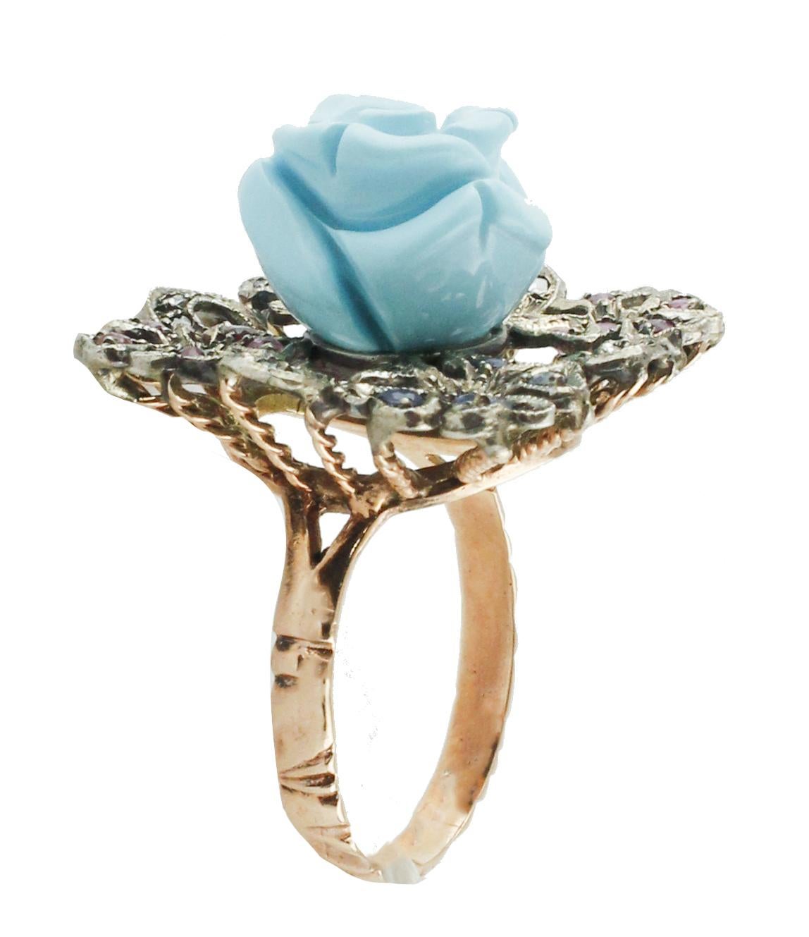 Cluster ring in 9K rose gold and silver composed by a torquoise paste flower in the center and four diamonds, blue sapphires and rubies flowers around it.
Diamonds 0.06 ct 
Blue Sapphires, Rubies 0.82 ct 
Torquoise paste 1.90 g
Total Weight 8.40