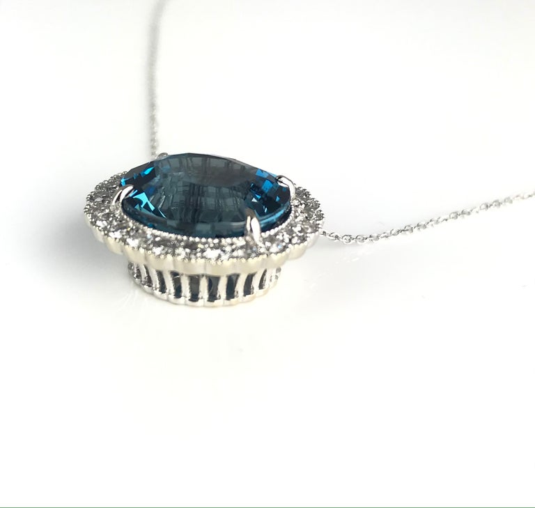 This beautiful pendant holds a 10.6 carat oval cut blue topaz, surrounded by 24 round diamonds in a halo (total weight 0.80 carats). Set in 14k White gold, with intricate milgrain work and a decorated under gallery, this pendant can surely give your