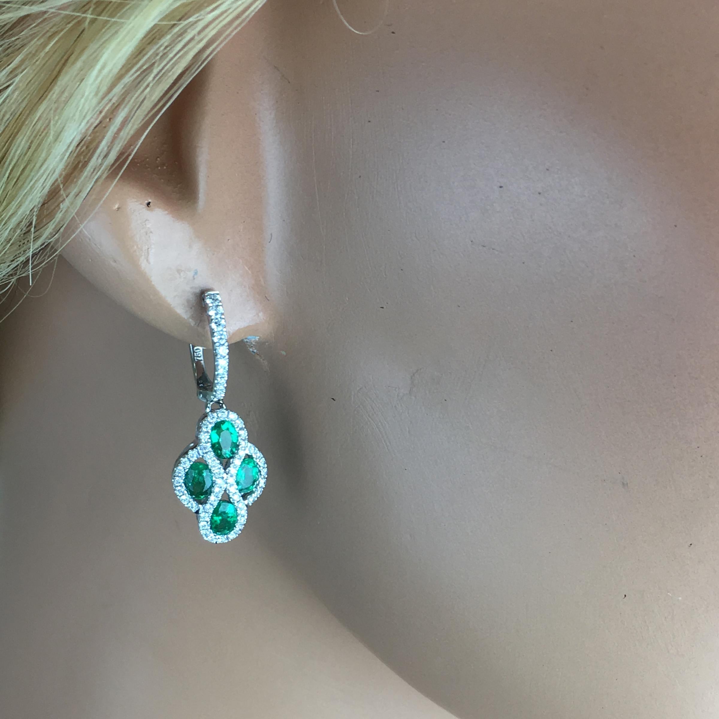 (DiamondTown) These lever-back dangle hoop earrings feature four oval cut fine emeralds (total weight 1.23 carats) surrounded by round white diamonds. Additional round diamonds lead up the front face of the hoop, bringing the total diamond weight to