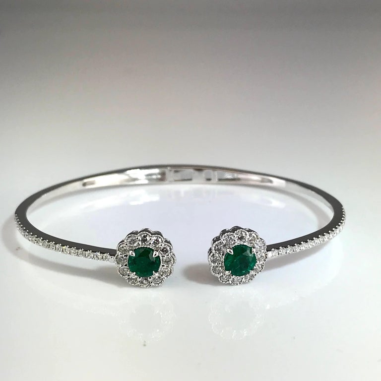 The heads on this bangle are two round cut emeralds, surrounded by a tight halo of round white diamonds, which also extends to the halfway point of the bangle. The heads of the bangle are also designed with delicate milgrain work to enhance the