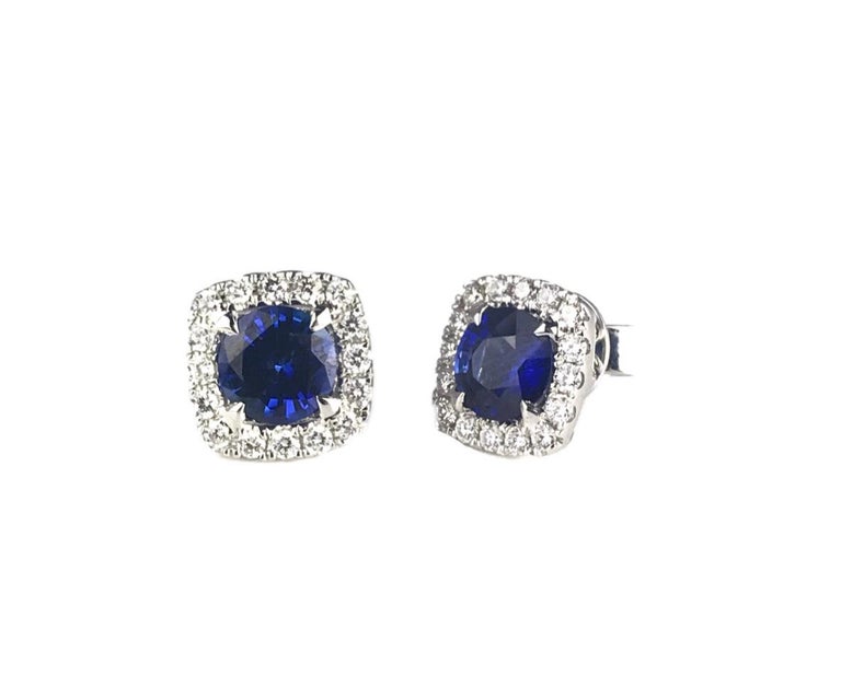 These earrings feature round cut sapphires inside a halo of round white diamonds. The overall appearance gives the impression of a cushion cut earring. The total sapphire weight is 1.92 carats. The diamond halo is 0.42 carats total weight. Set in