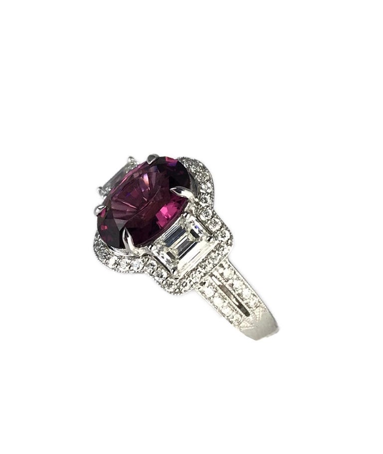 This ring has a 2.84 carat oval cut raspberry garnet center, flanked by two tapered baguettes and all surrounded by a border of round white diamonds. The trail of diamonds also trails down the sides of the ring.

Total garnet weight 2.84