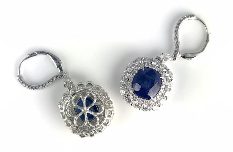 These stunning earrings hold 5.43 carat cushion cut sapphires, inside a double halo of round white diamonds. Additional diamonds decorate the front of the hoop. Each earring also features one pear shape diamond between the body of the earring and