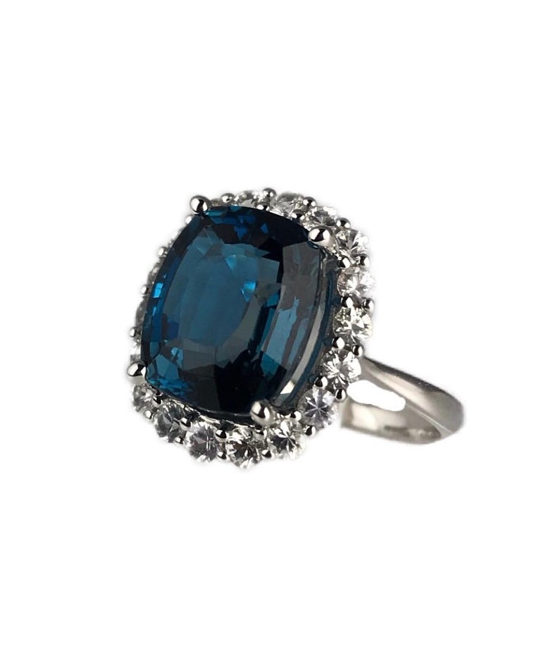 This gorgeous ring holds a 12mm x 10mm cushion cut London Blue Topaz center, surrounded in a halo of 18 round white sapphires. Set in 14k White Gold.

Total blue topaz weight - 7.29 carats
Total white sapphire weight - 1.03 carats

DiamondTown is