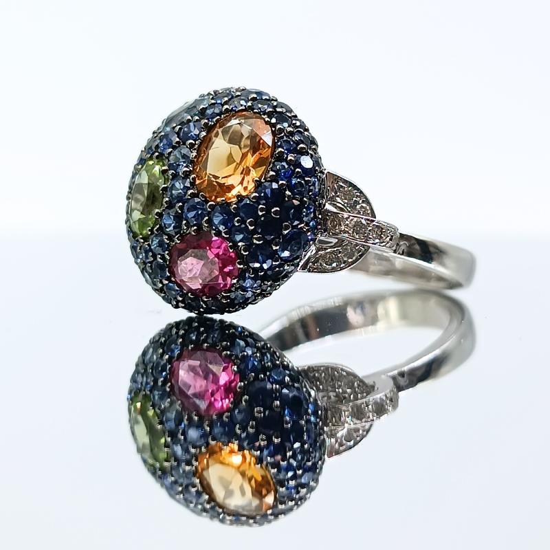 Diamrusa Ring in white gold.
Center Round shape with 83 Blue Shappires and different stones set 1 Citrine, 1 Peridot, 1 Pink Tourmaline and 1 Blue Topaz, decorations on the side with 20 Diamonds.

White Gold 18k
20 Diamonds 0.18k
83 Blue Sapphires