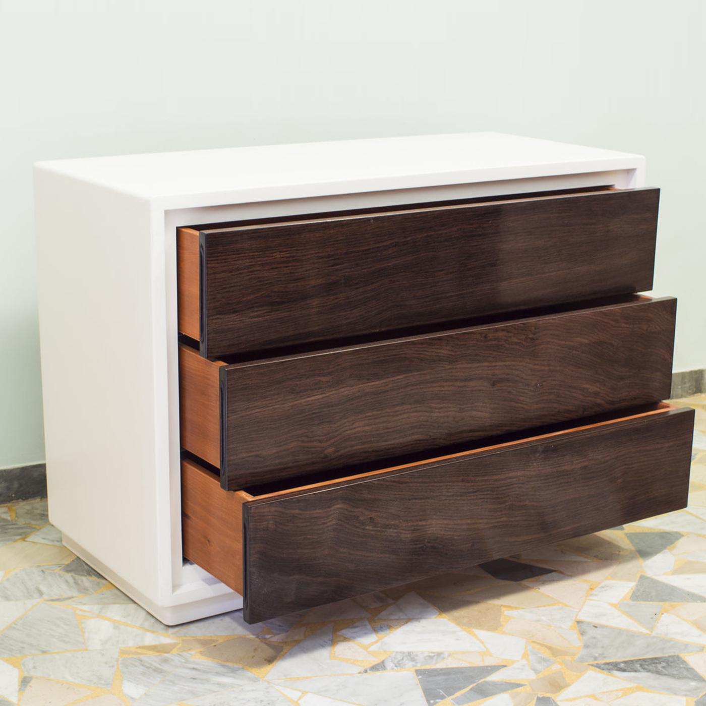Rich in storage potential, this large dresser exudes Art Deco glamour with its linear design and contrasting chromatic finishes. The blockboard wood frame with white-lacquered finish encloses three handle-free beechwood drawers with shellacked