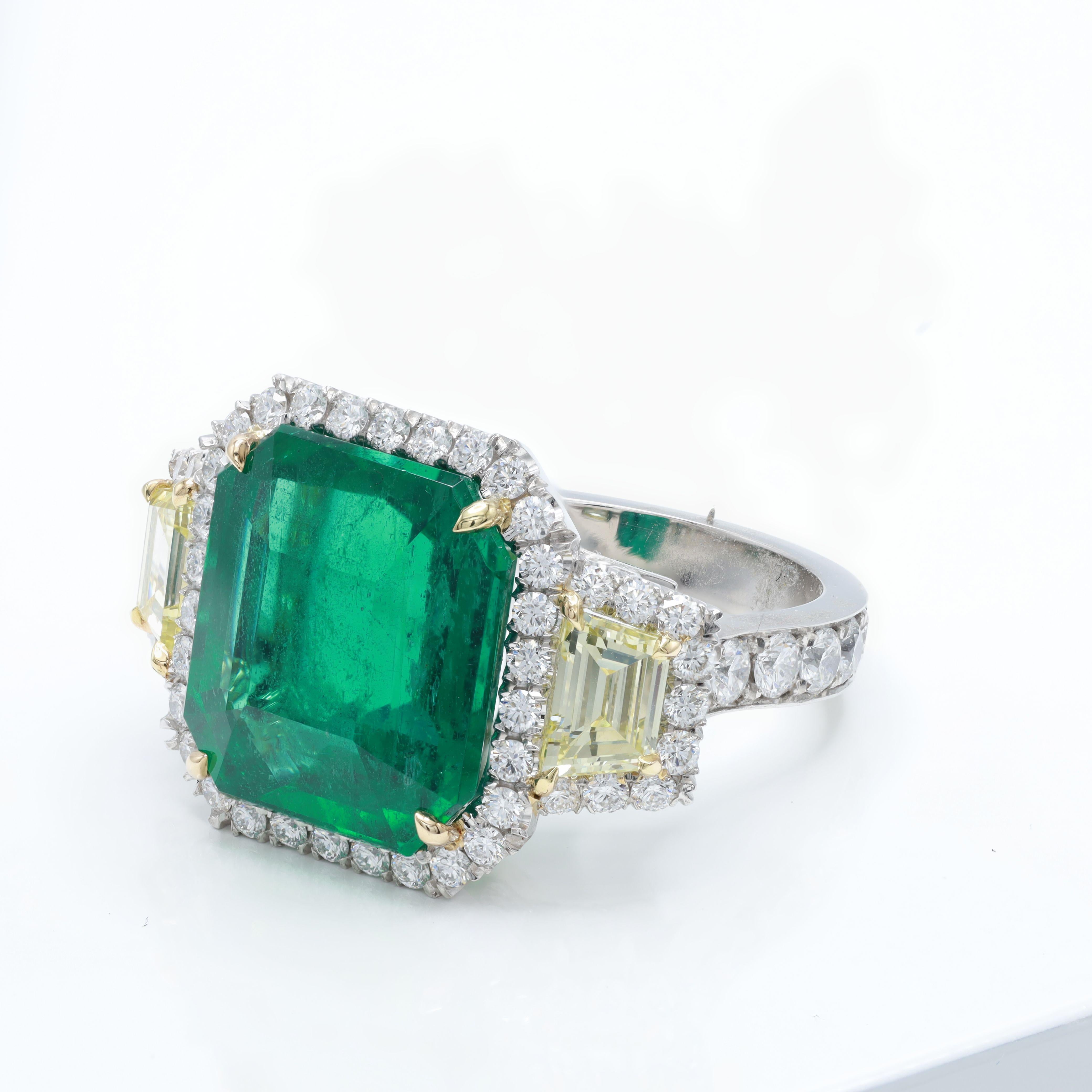 Platinum and 18 kt yellow gold emerald and diamond ring featuring a 10.13 ct green emerald alongside 2 step cut  trapezoids totaling 1.21 cts set in a halo setting totaling 1.65 cts