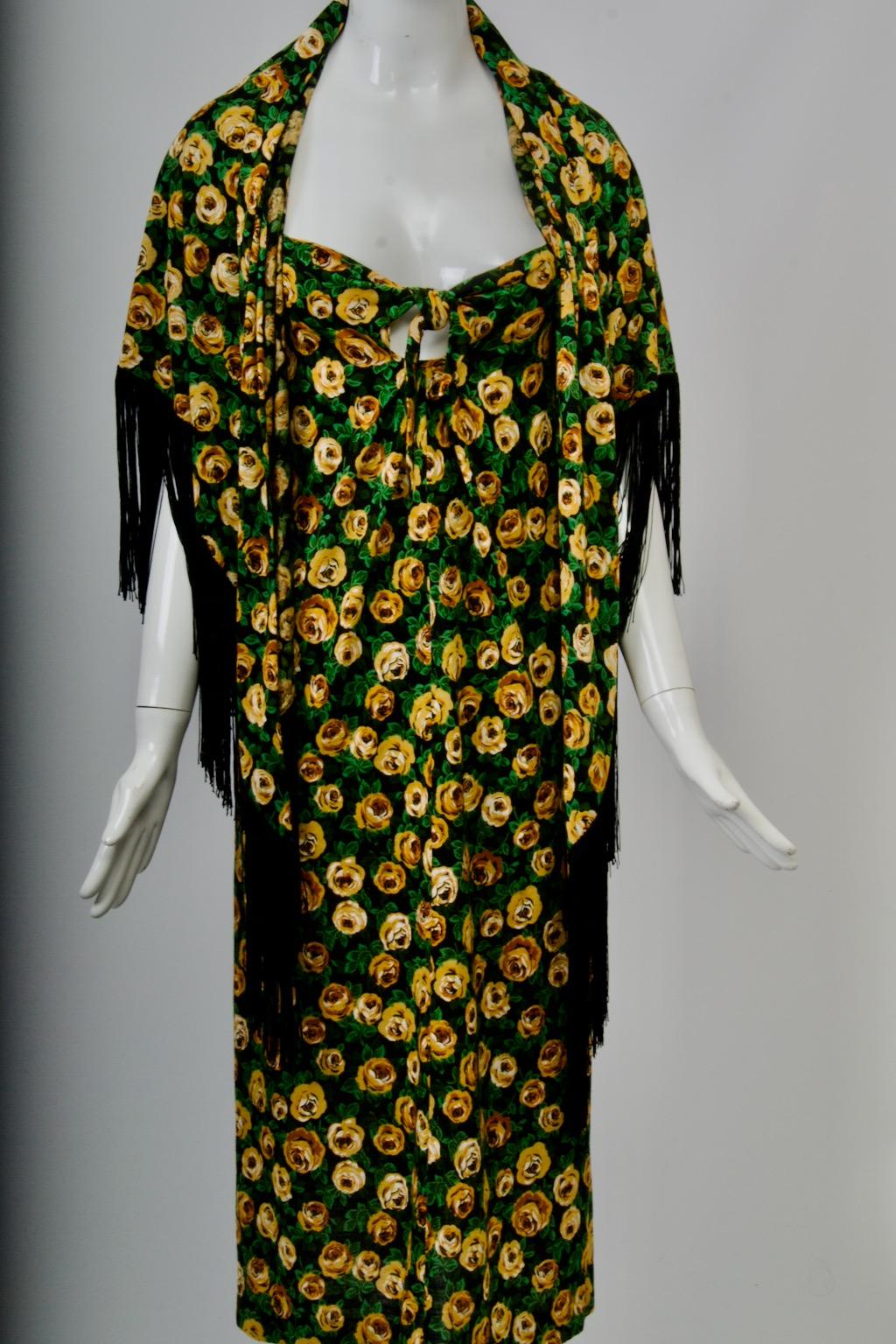 Diane von Furstenberg maxi dress, c.1970s, its allover floral print of varied gold-tone flowers and green leaves against a black background. Accompanying the dress is a deep, rounded shawl of the same pattern trimmed with black fringe. The dress