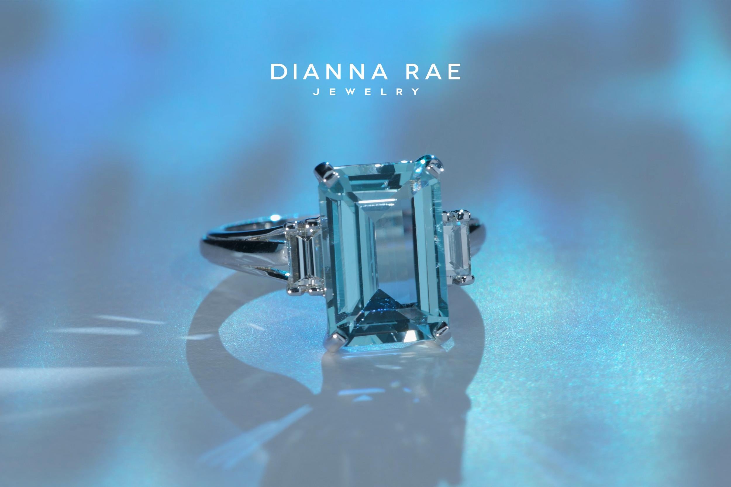 This three stone ring is studded with an emerald-cut Aquamarine and two baguette Diamonds. The sparkling diamonds beautifully highlight the center stone. Exuding a refined and opulent look, this prong set aquamarine and diamond ring is designed in