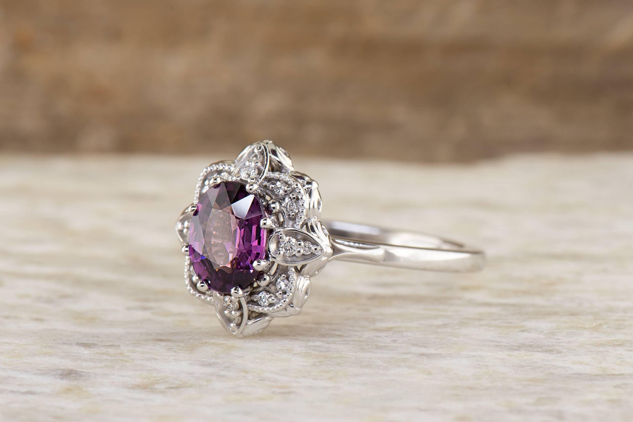 This 14K white gold ring shines with beautiful floral and vintage design elements. In the center is a 1.31 carat oval faceted grape garnet. In the midst of all of the milgrain and floral design work is 0.11 carat total weight diamonds.