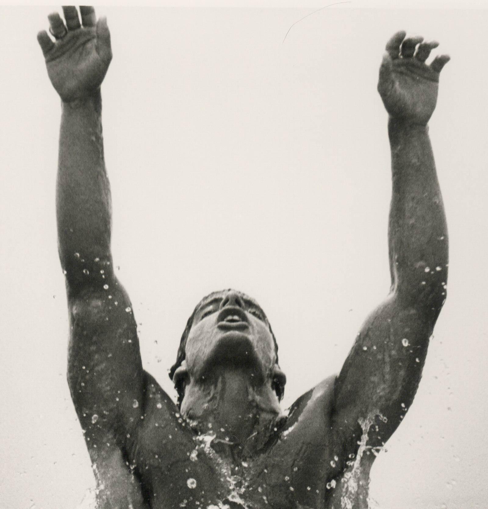 Kenny Surfacing (jeune homme nu sautant hors de la mer les bras levés vers le ciel) - Photograph de Dianora Niccolini