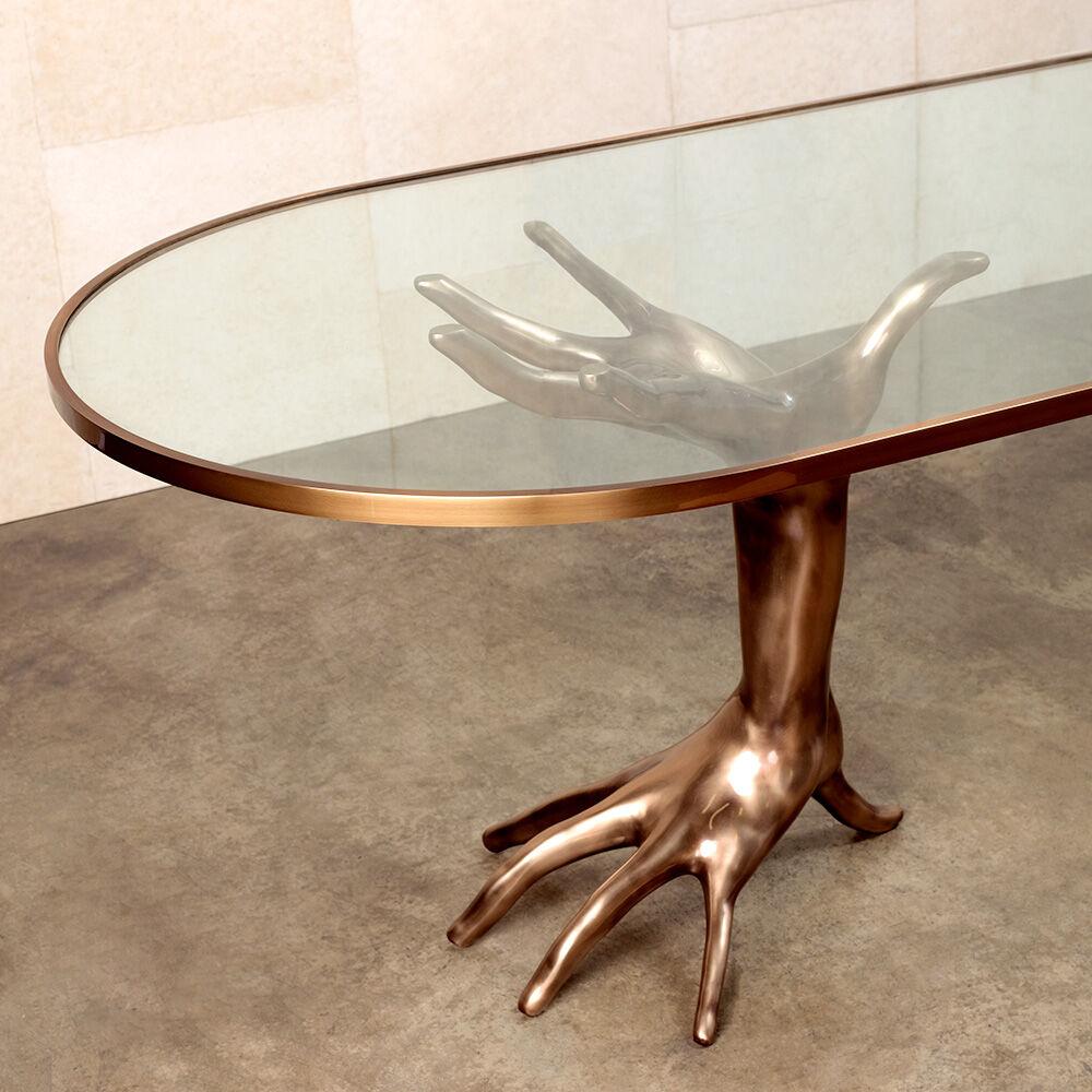 The luxurious and sculptural Dichotomy racetrack dining table is a stunning and unique statement table inspired by classical figurative decor. The two bases are cast in bronze and meticulously polished by hand. The tempered glass racetrack-shaped