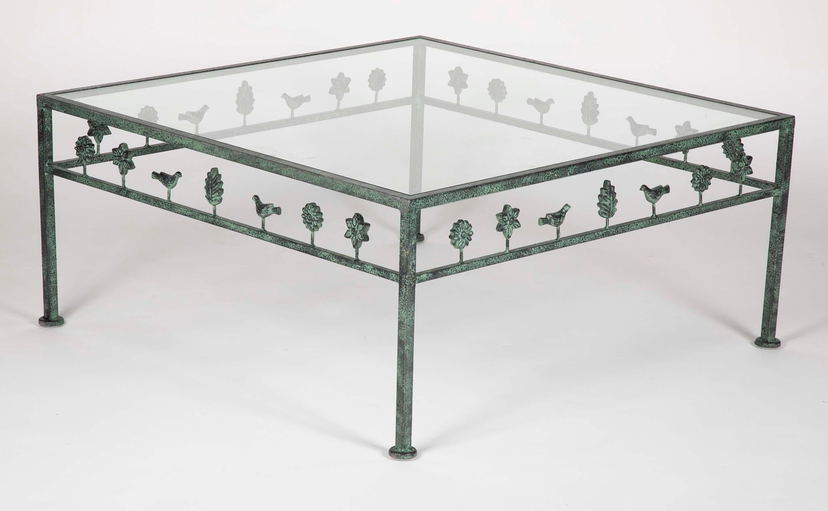 A handsome glass topped coffee or cocktail table in the style of Diego Giacometti. The sides decorated with trees, birds and flowers with an enameled surface in black and verdigris green.