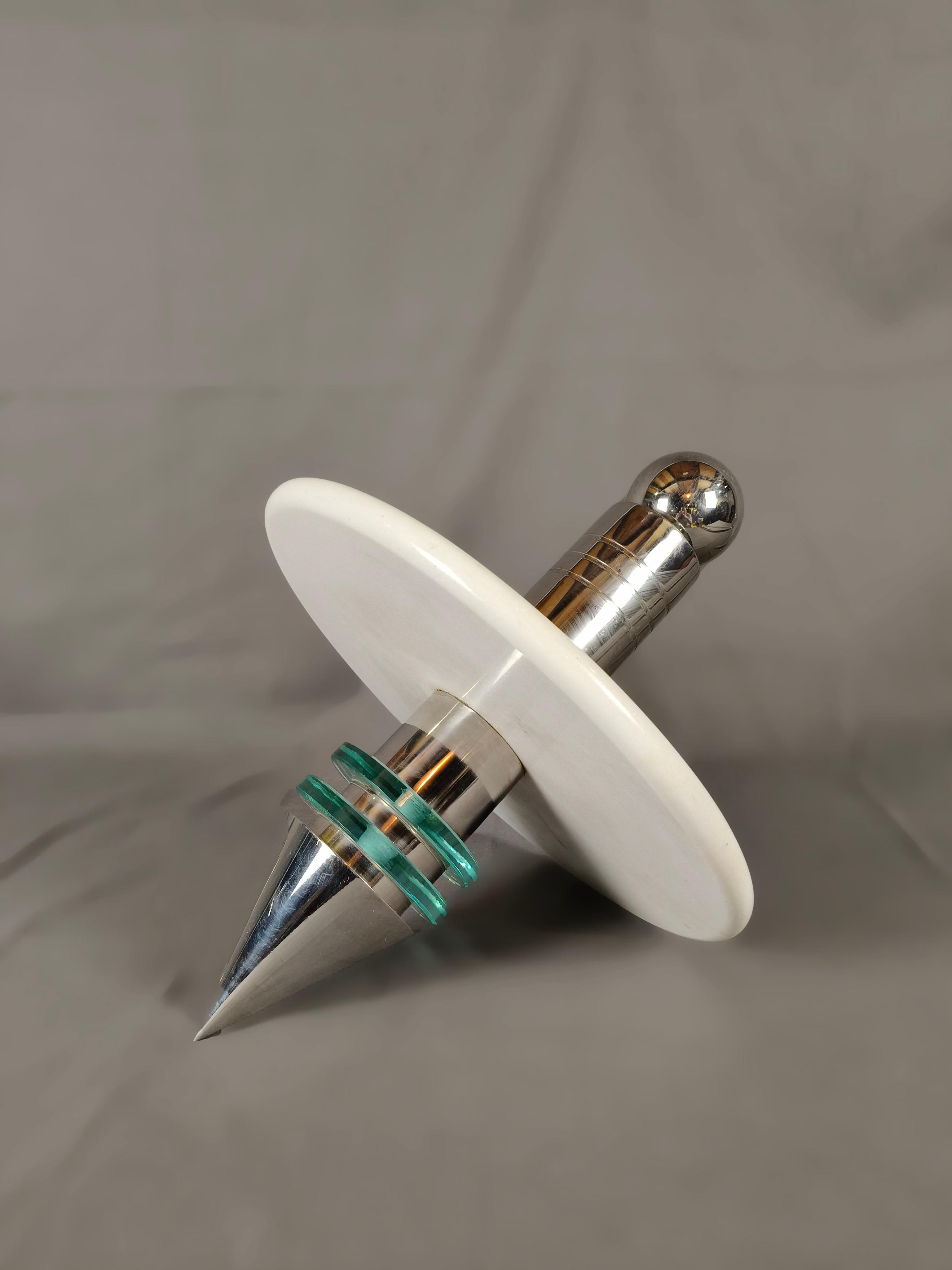 Una pesante trottola messicana degli anni '70 in cromo, marmo e vetro dell'artista messicano Diego Matthai. La struttura cromata è circondata da due anelli di vetro vicino all'estremità tagliente. Il grande disco di marmo bianco è l'aggiunta più