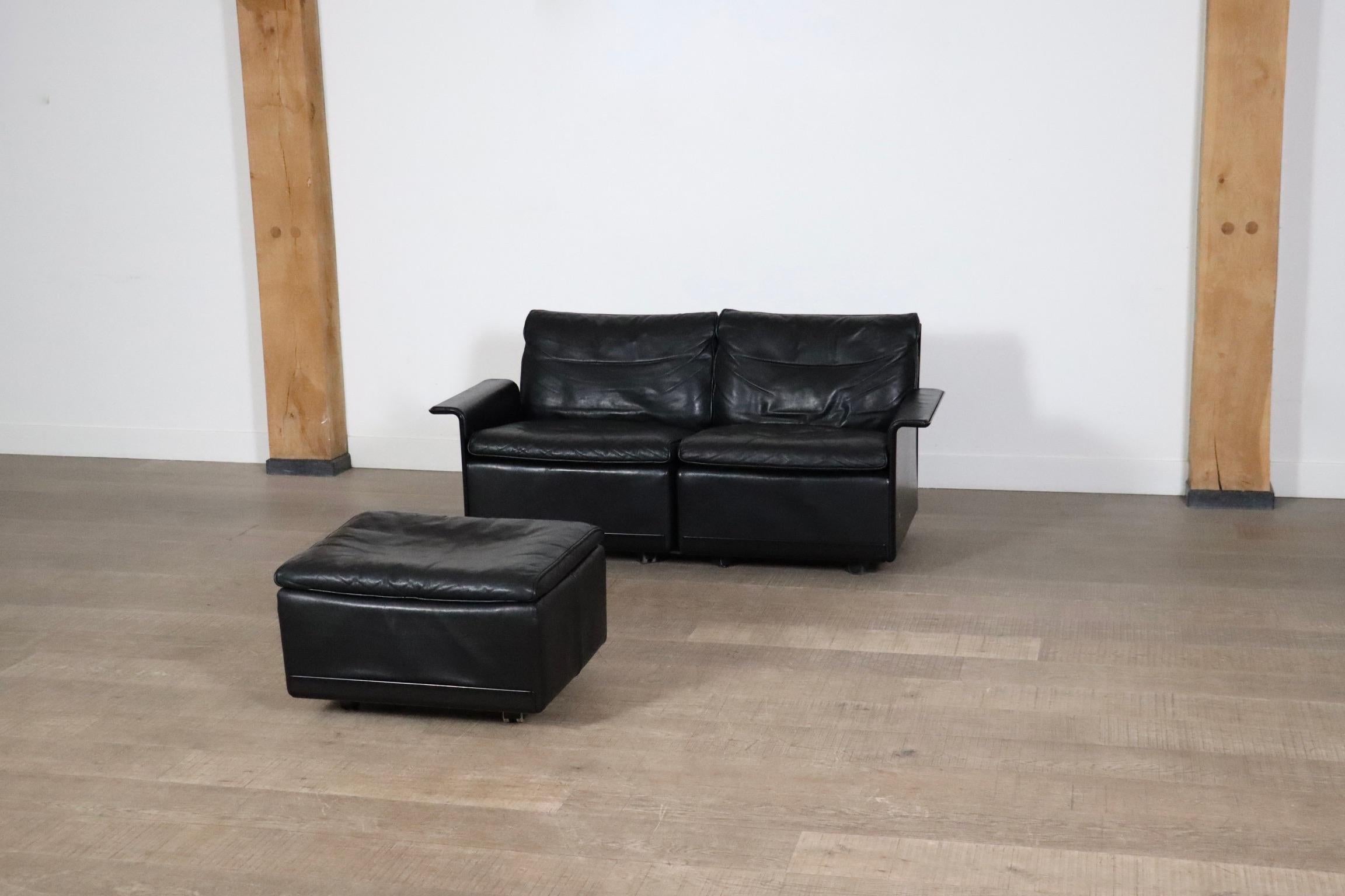 Schönes Zweisitzer-Sofa mit Ottomane in schwarzem Leder von Dieter Rams für Vitsoe. Die schwarze Außenhülle besteht aus einer heißgepressten Formmasse, die ähnlich wie Glasfaser ist, aber stärker als diese. Dieses Sofa ist aus hochwertigem schwarzem