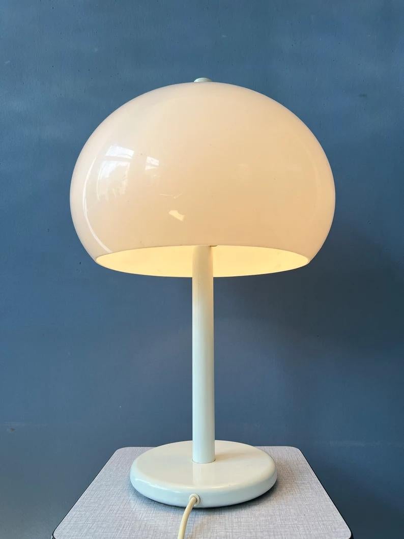 Lampe de table Dijkstra blanche avec abat-jour en forme de gros champignon. L'abat-jour en verre acrylique blanc produit une lumière agréable et chaleureuse. La lampe nécessite une ampoule E27/26 (standard) et dispose actuellement d'une fiche de