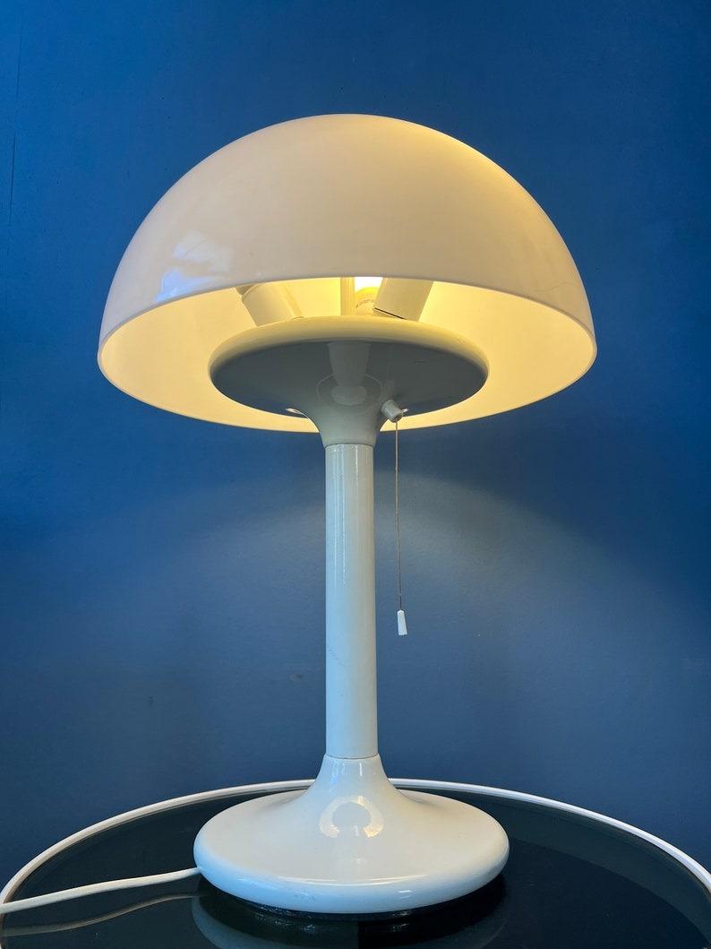 Lampe de table en plexiglas à champignon blanc Dijkstra. L'abat-jour en verre acrylique blanc produit une lumière agréable et chaleureuse. La lampe nécessite une ampoule E27/26 (standard) et dispose actuellement d'une fiche de connexion à