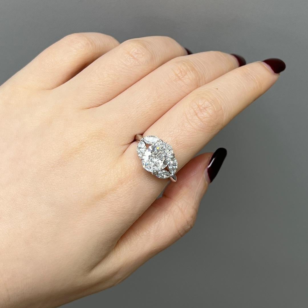 A classic and charming diamond ring, showcasing a 2.54 carats oval cut diamond certified by GIA as D Color and SI1 clarity, set on a classic eight prong diamond-encrusted basket setting. Flanked by four collection color marquise diamonds weighing