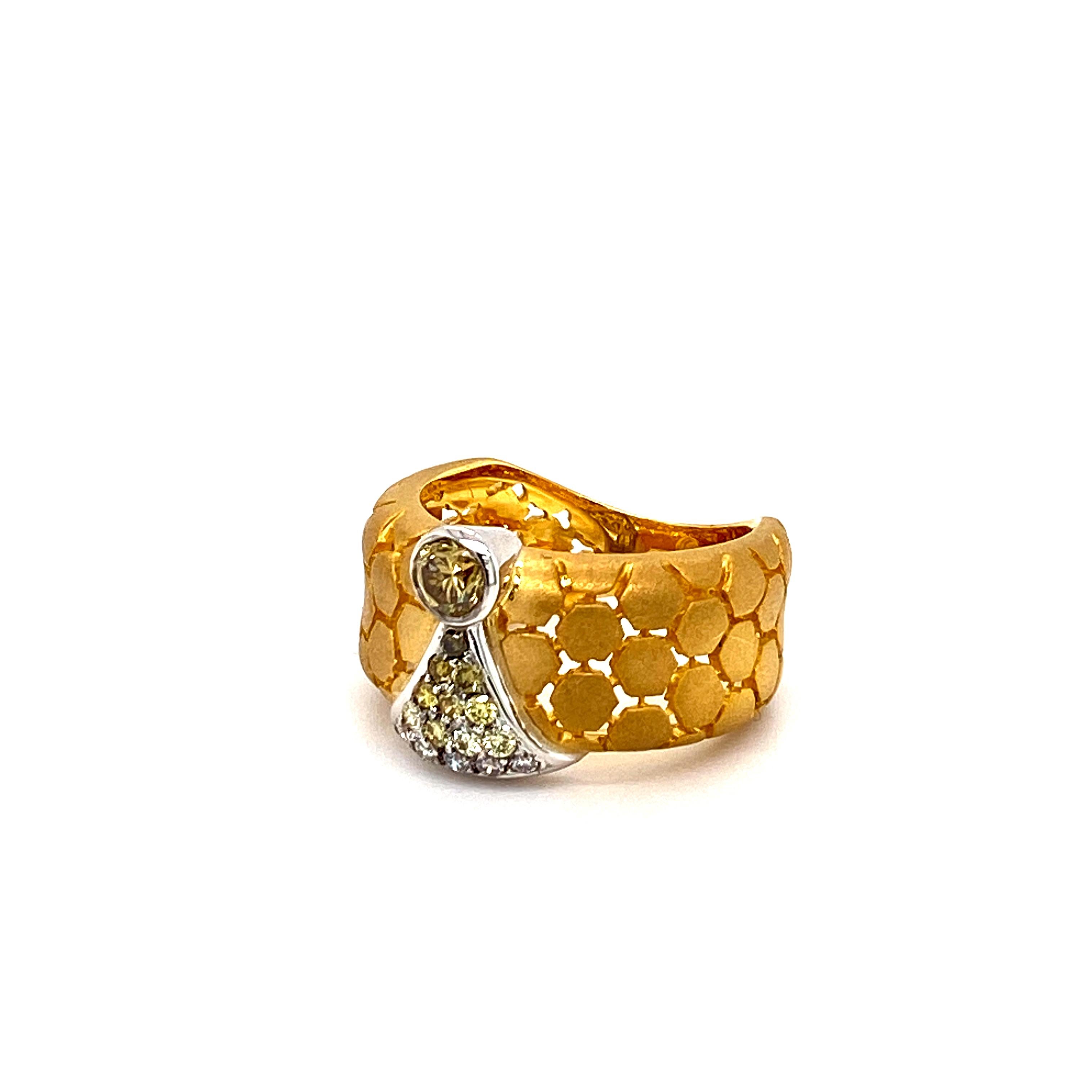 Cette bague en or 18 carats à la finition mate présente un motif en nid d'abeille avec une pierre centrale en diamant rond de couleur fantaisie et de taille brillante, suivie d'un dégradé étincelant de 15 diamants plus petits, sertis en pavé, qui