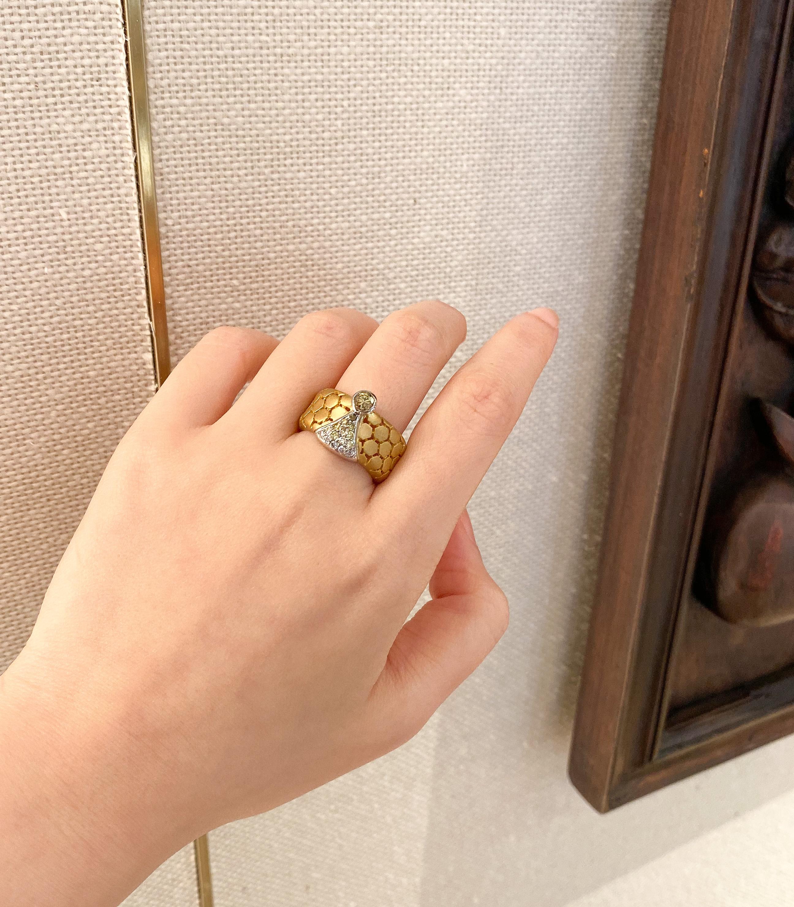 This 18 karat gold ring with matte finishing features a honeycomb pattern with a fancy color round brilliant cut diamond center stone, followed by a sparkling gradient of 15 smaller, pavé-set diamonds that graduate from fancy color to white round